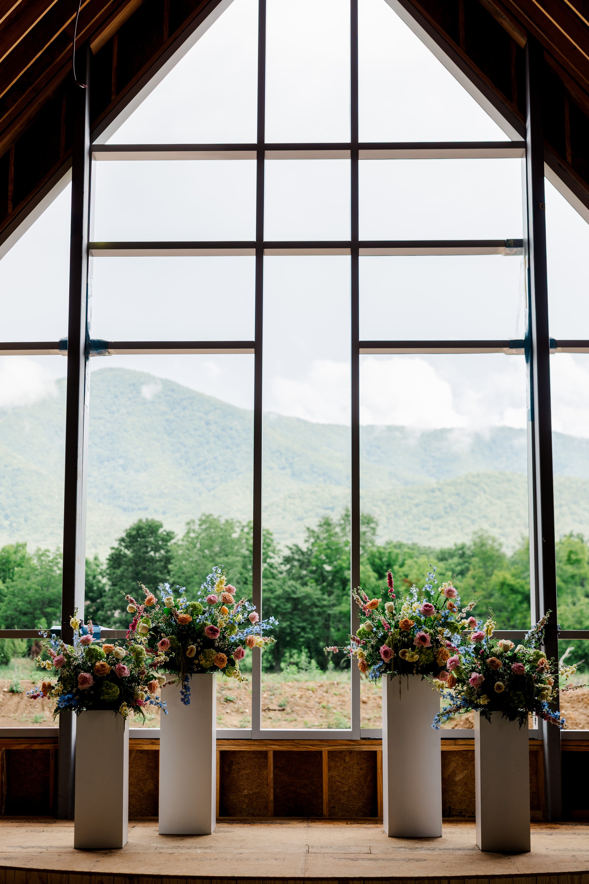 Interior construction progress at The Lumigail chapel, featuring floor-to-ceiling windows, floral arrangements, and Smoky Mountain views near Pigeon Forge, Tennessee.