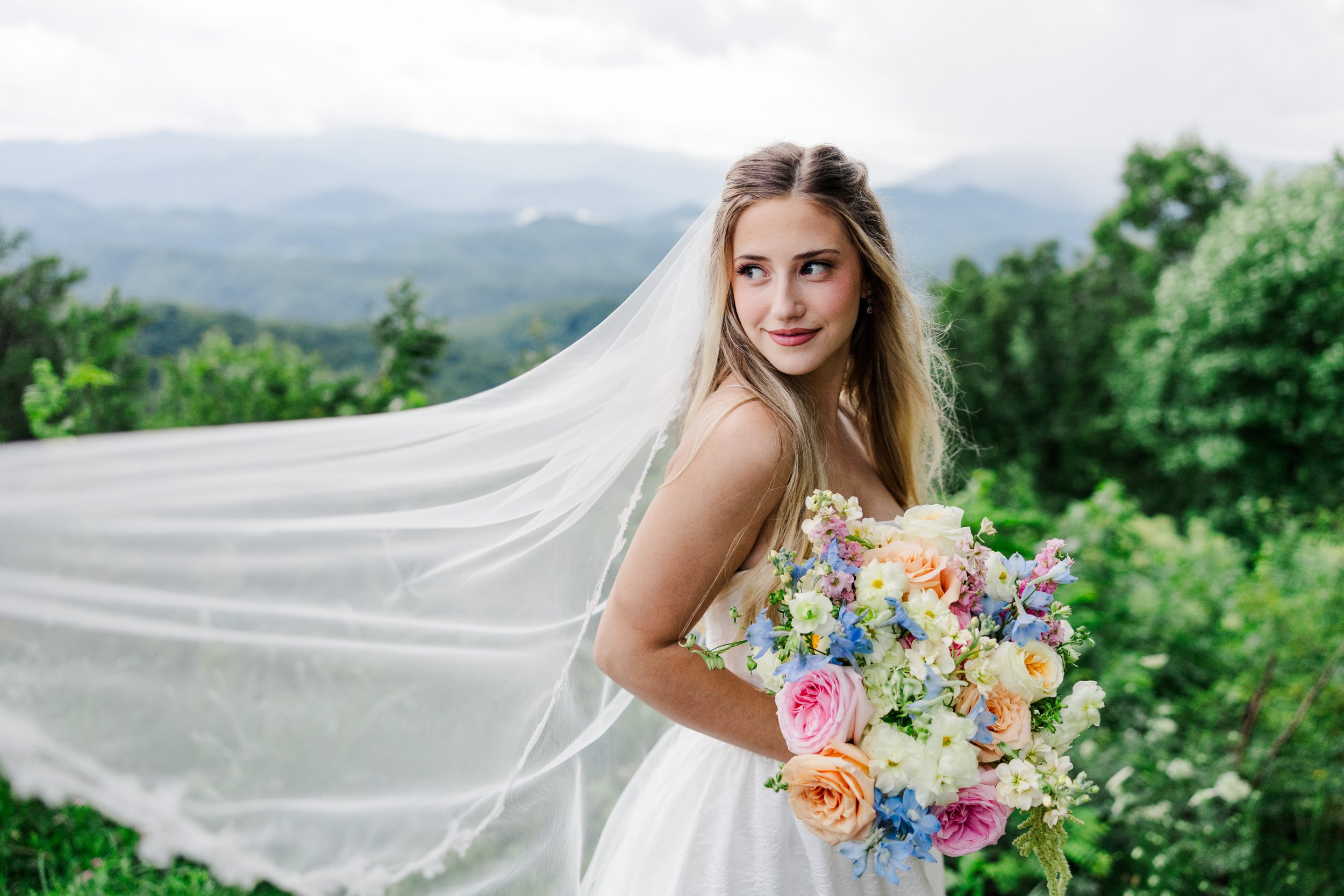 Bride with a flowing veil and colorful bouquet overlooking the Smoky Mountains at The Lumigail wedding venue in Wears Valley, Tennessee.