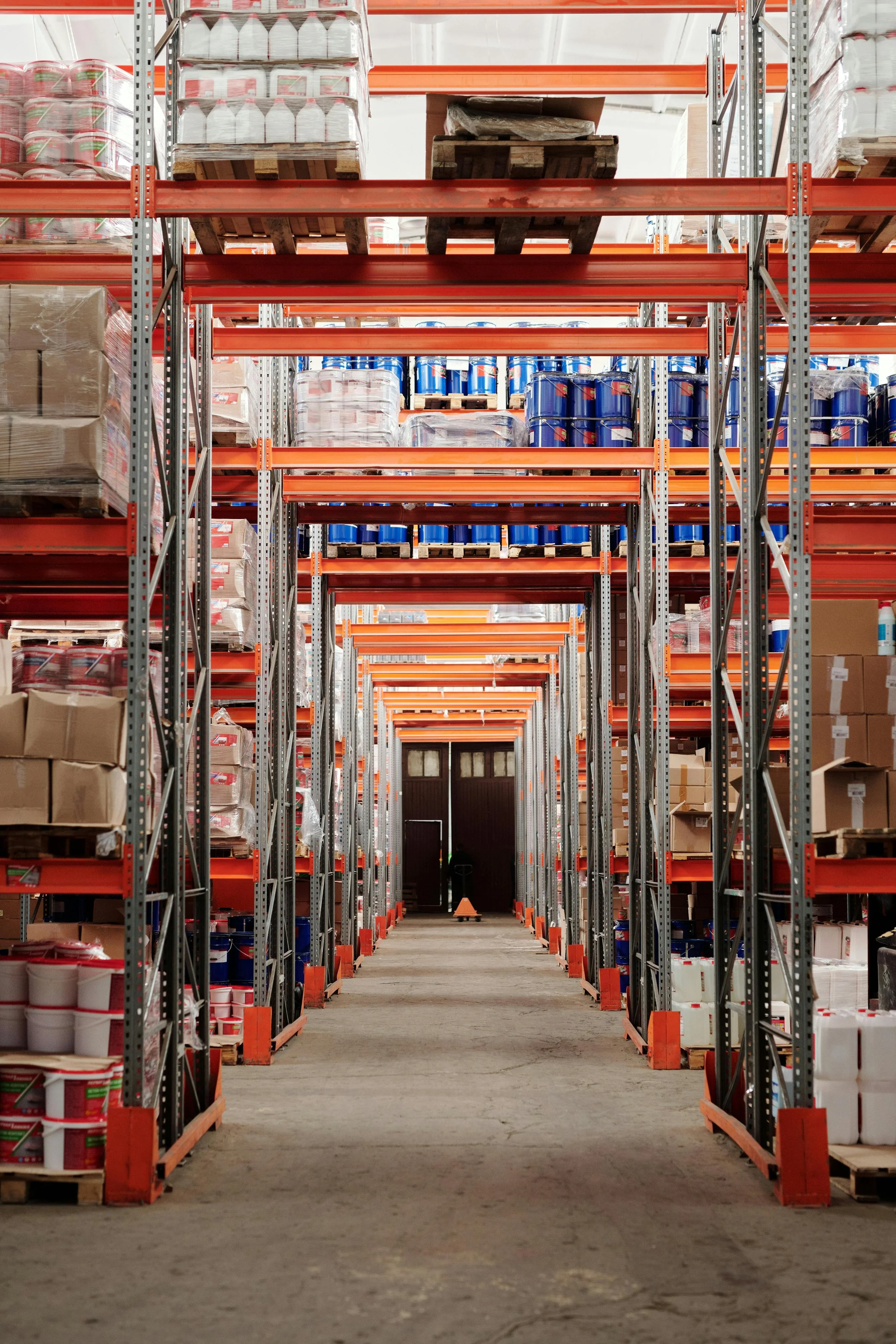 Industrial warehouse aisle with metal shelving stocked with various packaged goods and supplies.