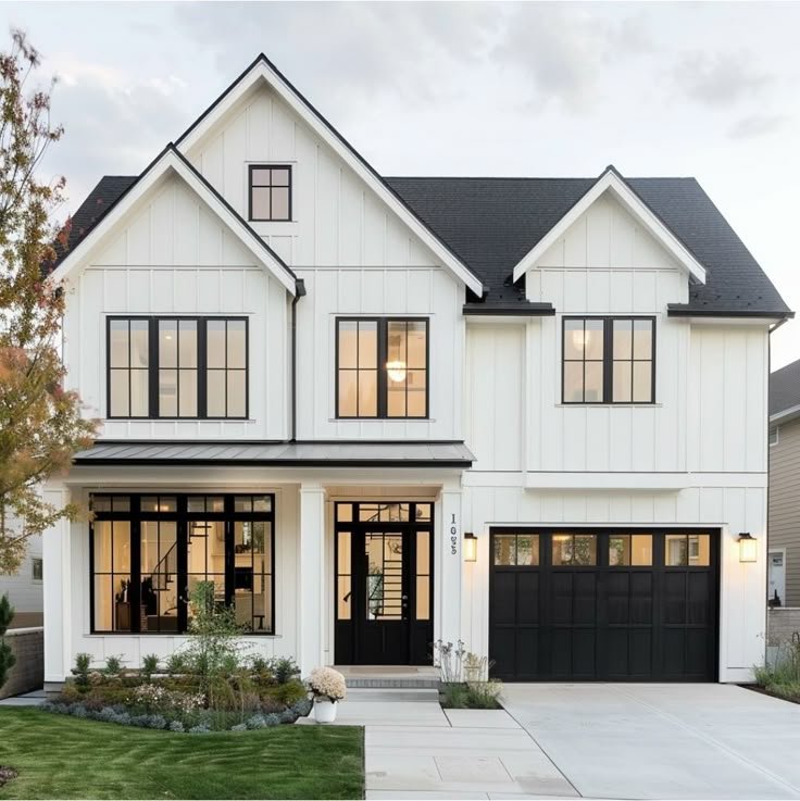 Modern two-story house with white exterior, black window frames and garage door, large front windows, and a well-maintained lawn.