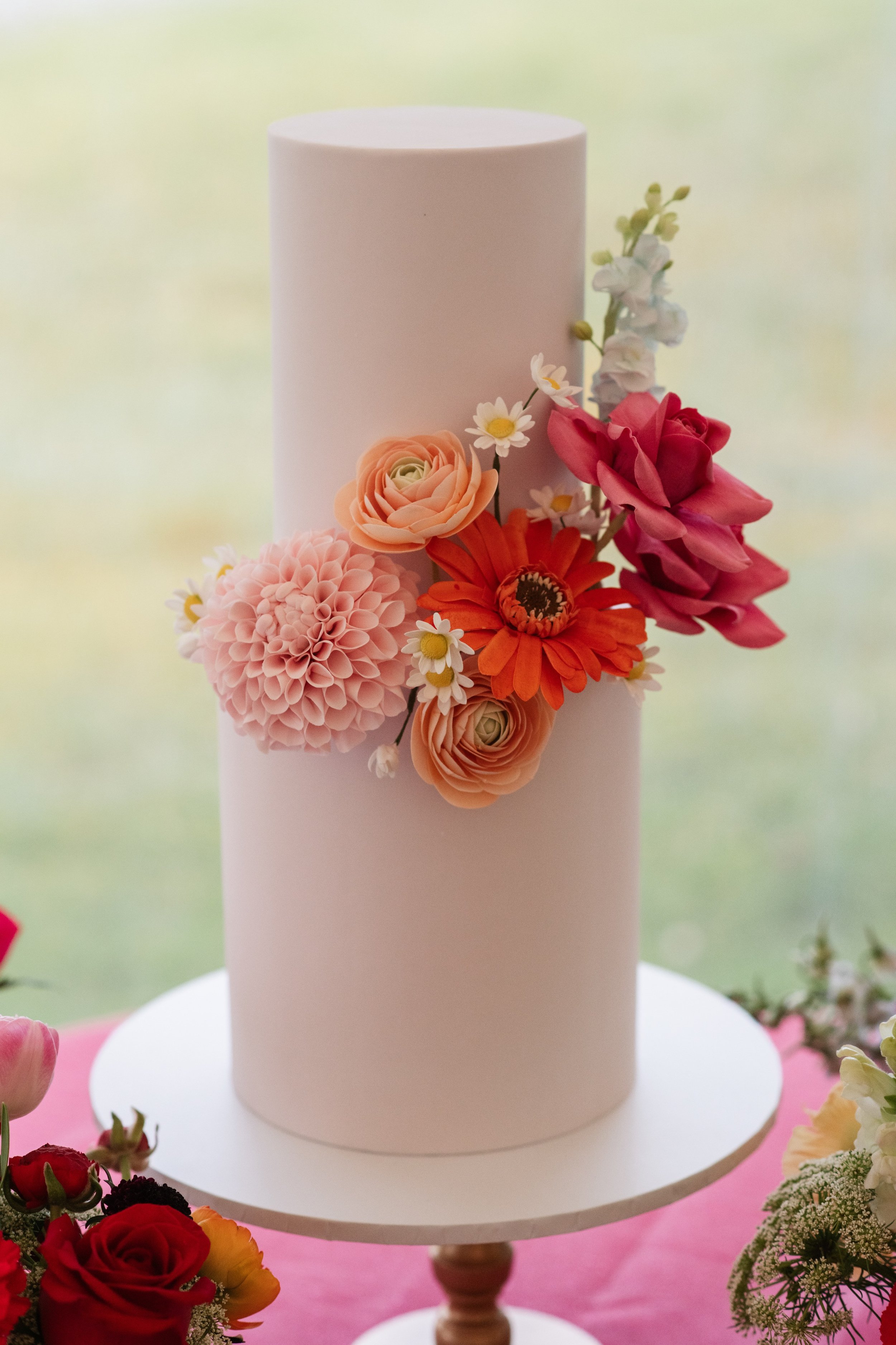 A tall white cake decorated with a cluster of pink, peach, orange, and white artificial flowers.