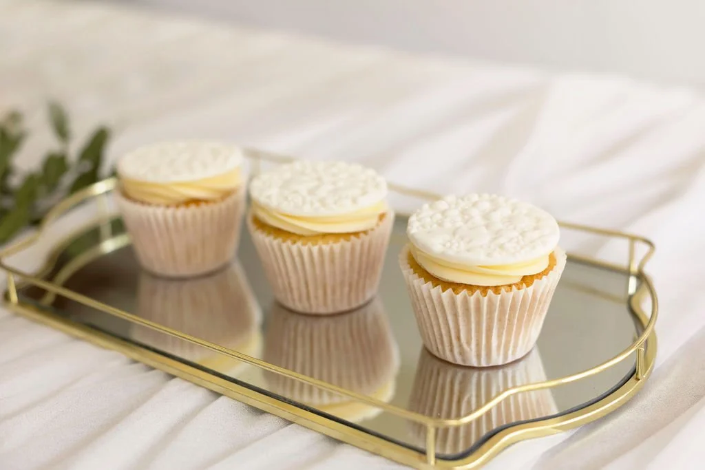 Three cupcakes with white frosting and decorative white sprinkles on a mirror tray.