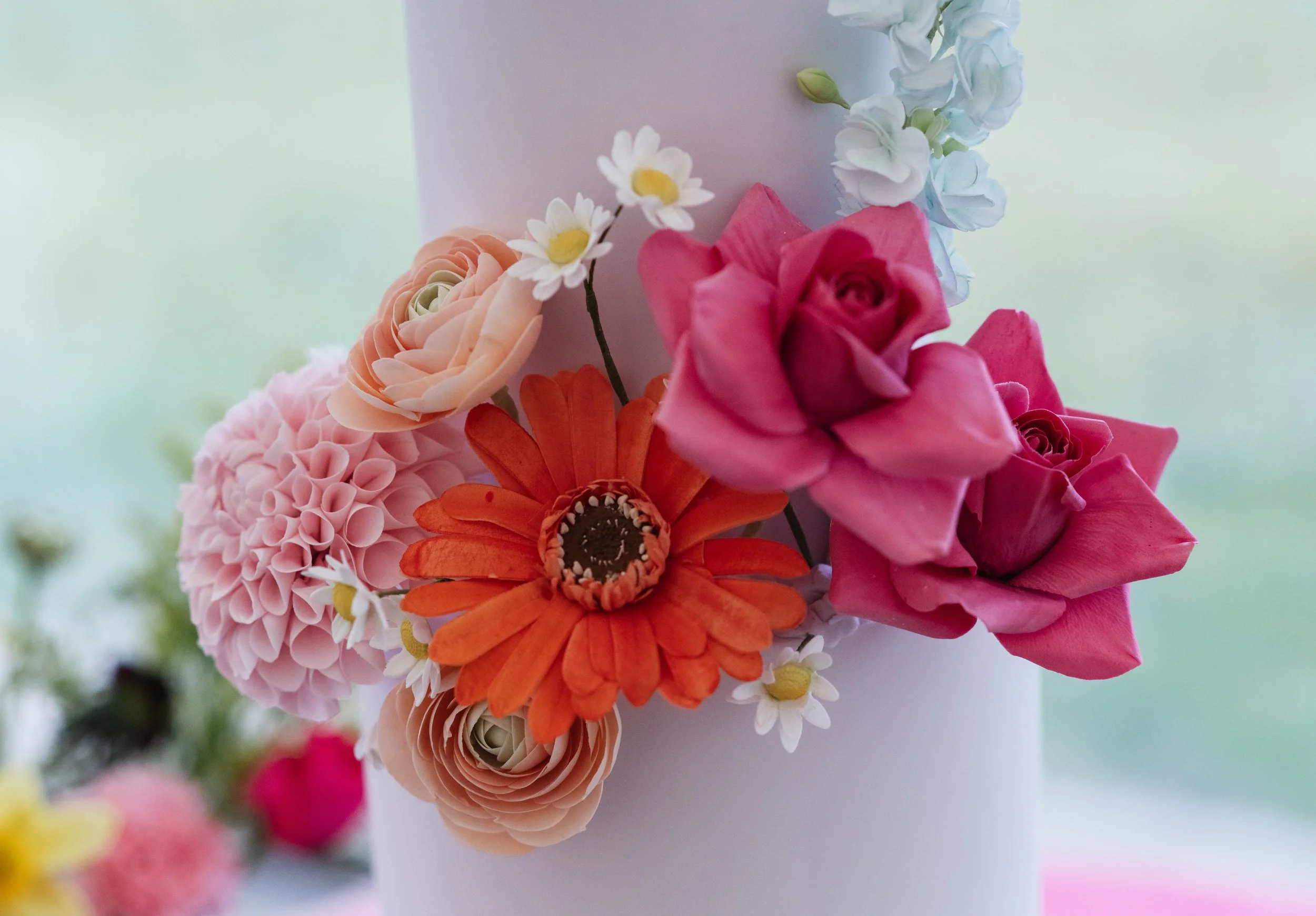 Close-up of a bouquet of pink, orange, and cream flowers, with some white daisies, attached to a light-colored background