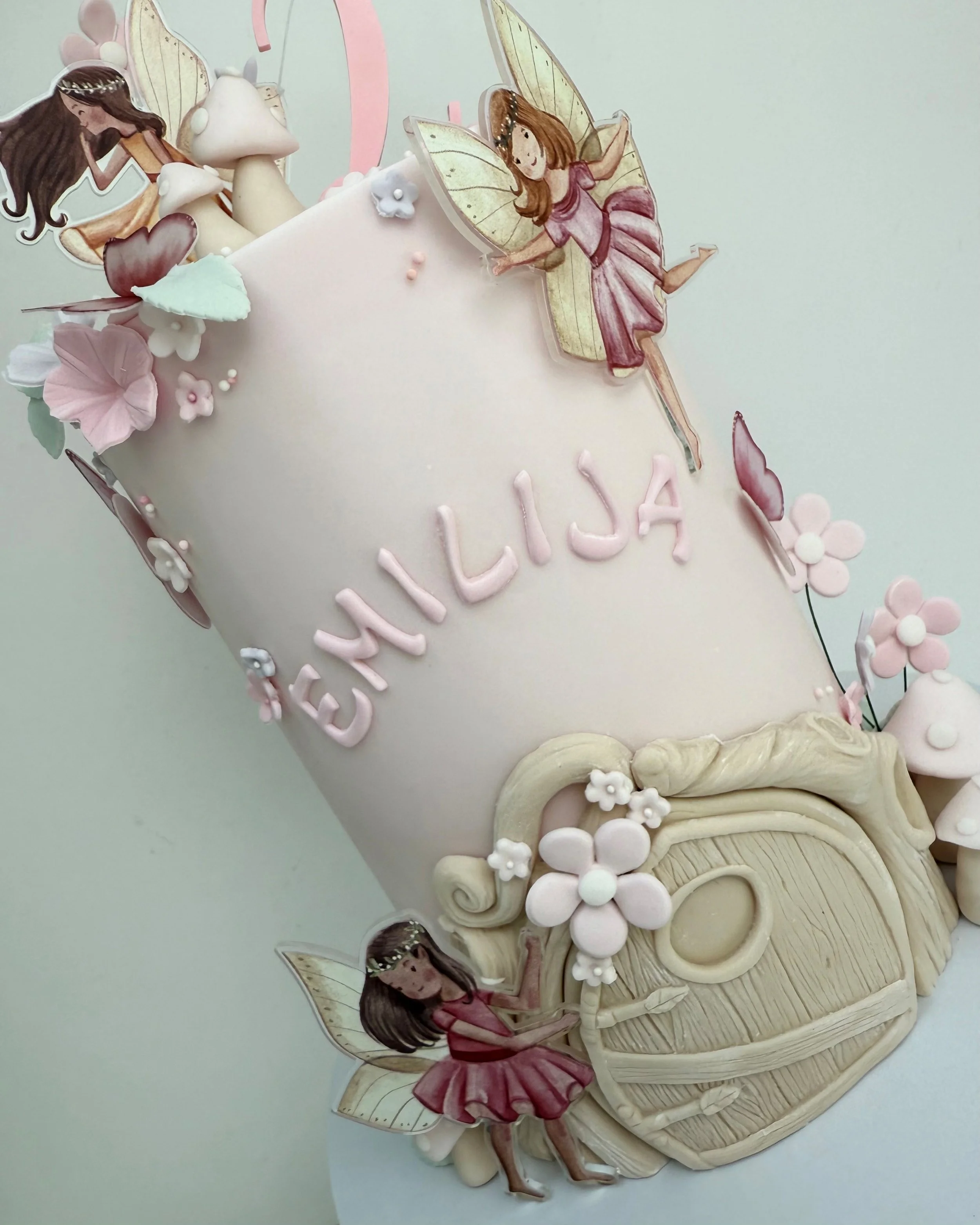 Decorative cake with fairy and flower motifs, featuring the name 'EANELIA' written on it.