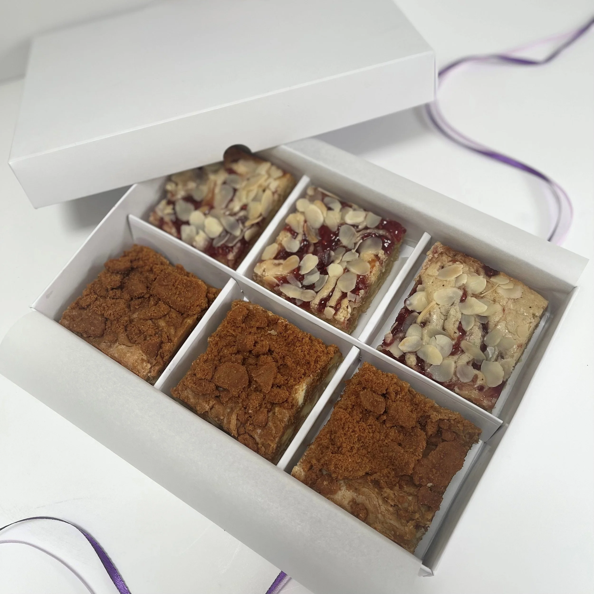 Open box of six assorted dessert bars on a white surface.
