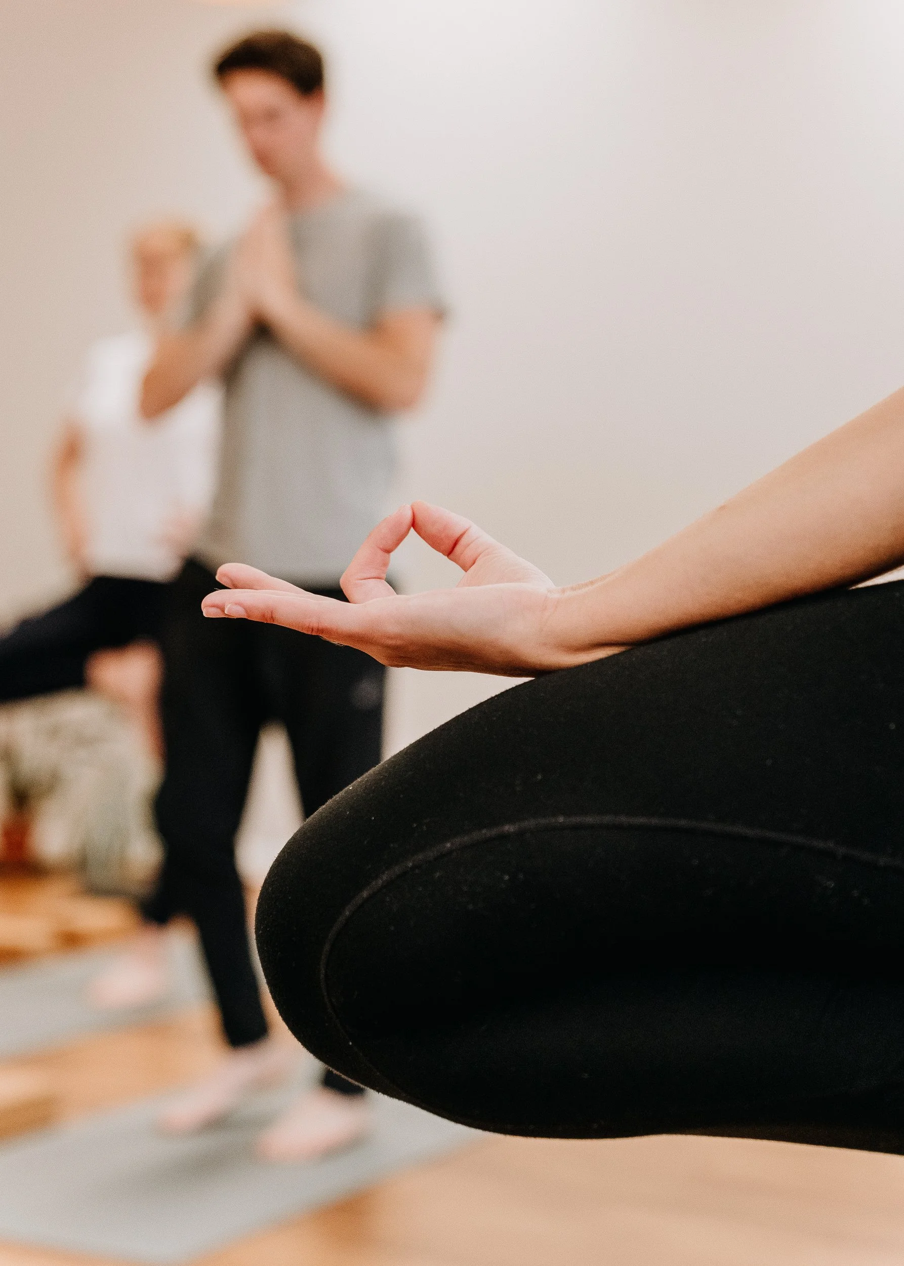 Close-up of a person meditating in the foreground with a yoga pose, with a blurred person in the background at Every Body Studio in Oxford