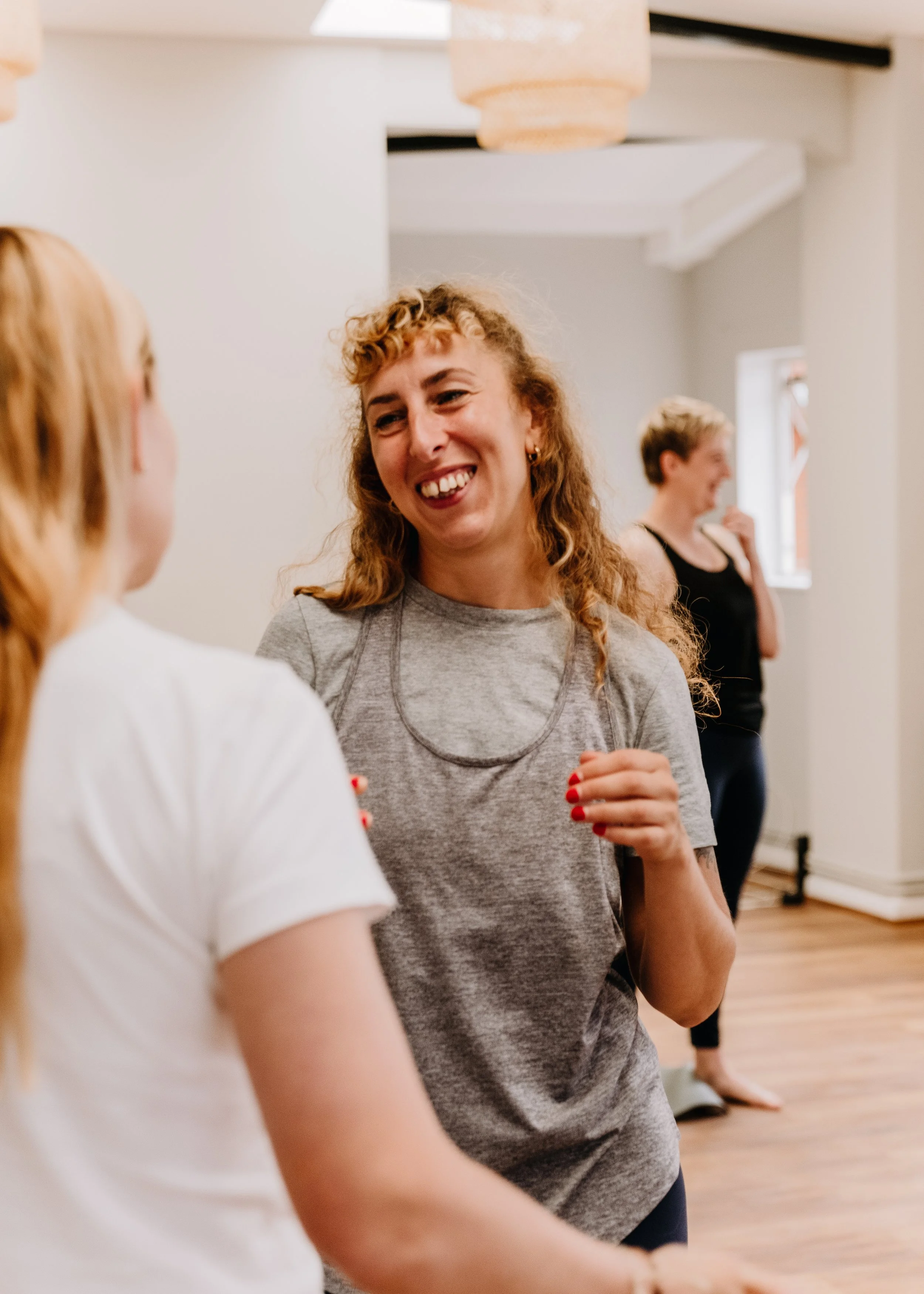Three women smiling and talking at Every Body Studio in Oxford, two in the foreground and one in the background.