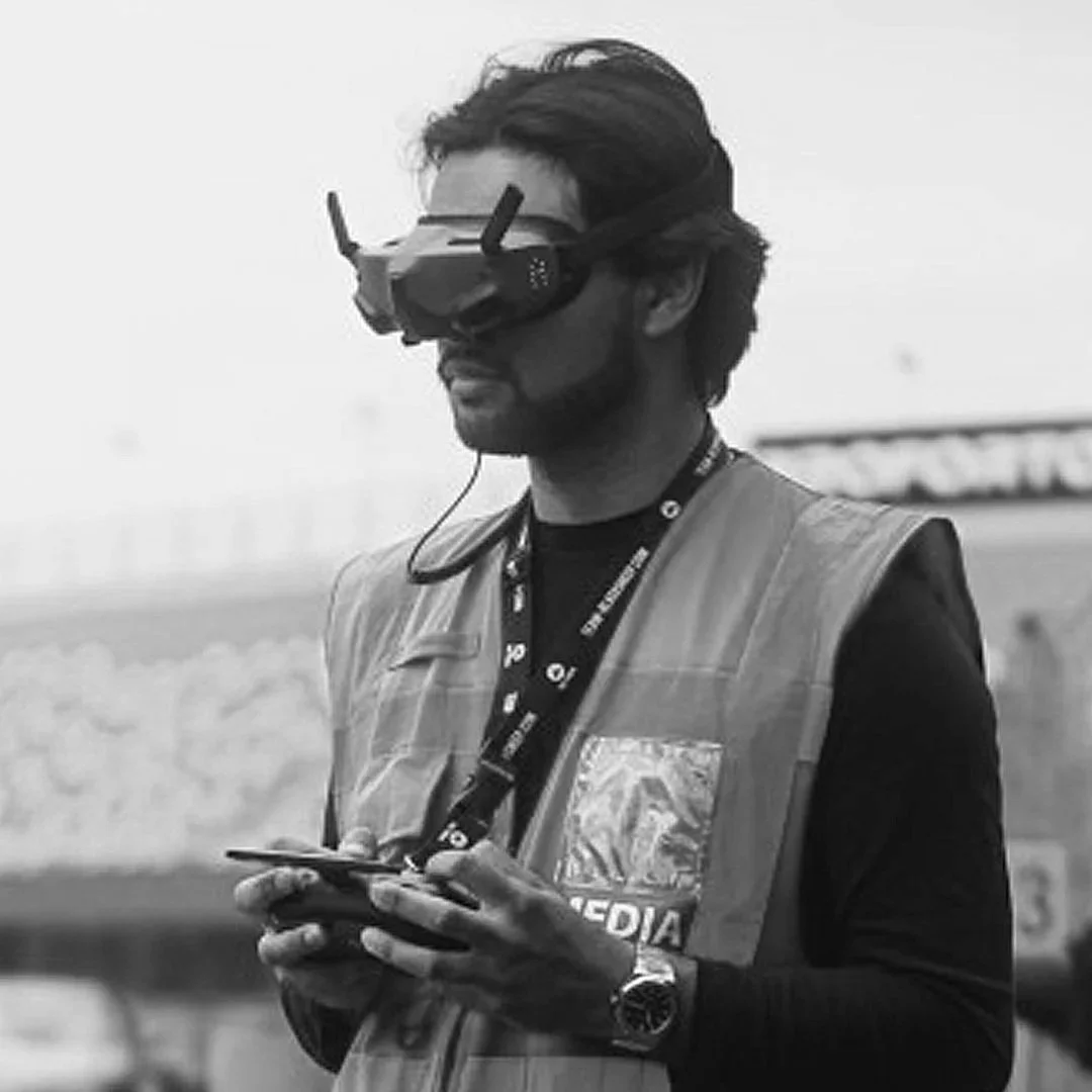 A man wearing a virtual reality headset, a media badge, and a reflective safety vest, holding a smartphone, standing outdoors.