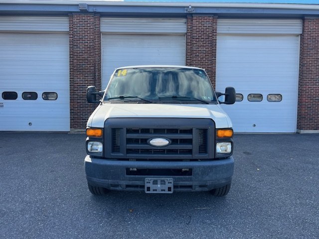 Front view of a white Ford cargo van parked in front of a brick building with three closed garage doors.
