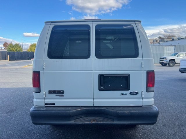 Rear view of a white Ford E-250 van parked in a parking lot under a partly cloudy sky