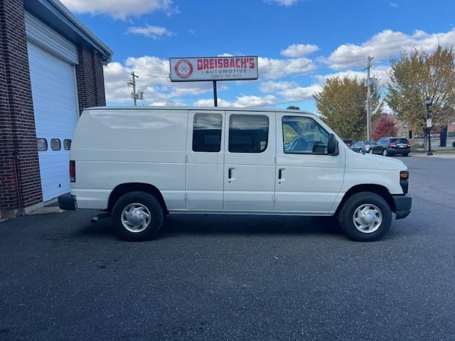 White van parked outside a brick building with a sign that reads 'Dreisbach's Automotive' and a cloudy blue sky in the background.