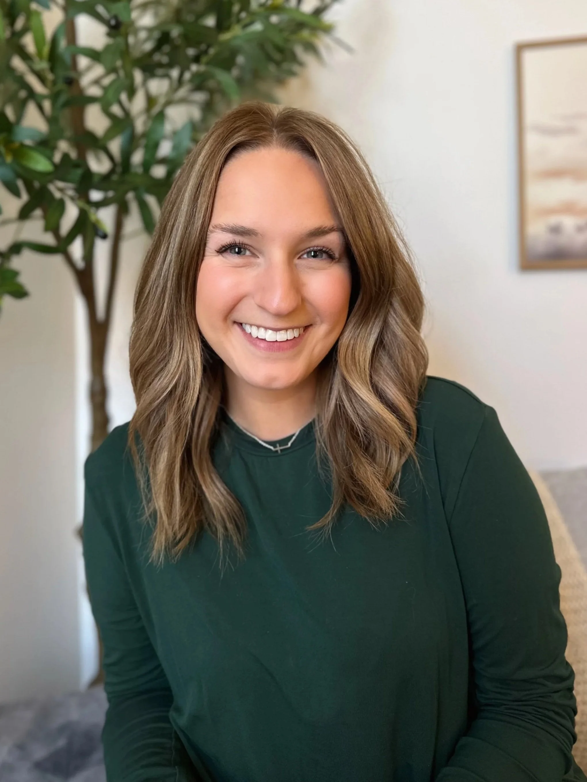 A smiling woman with brown, wavy hair wearing glasses and a black top.