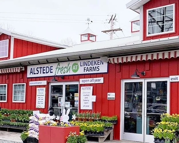 Exterior of Alstede Fresh at Lindeken Farms red farm market with flowers for sale in front.