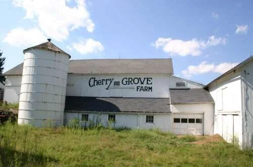 White barn on a clear sky day with "Cherry Grove Farm" written on the exterior.