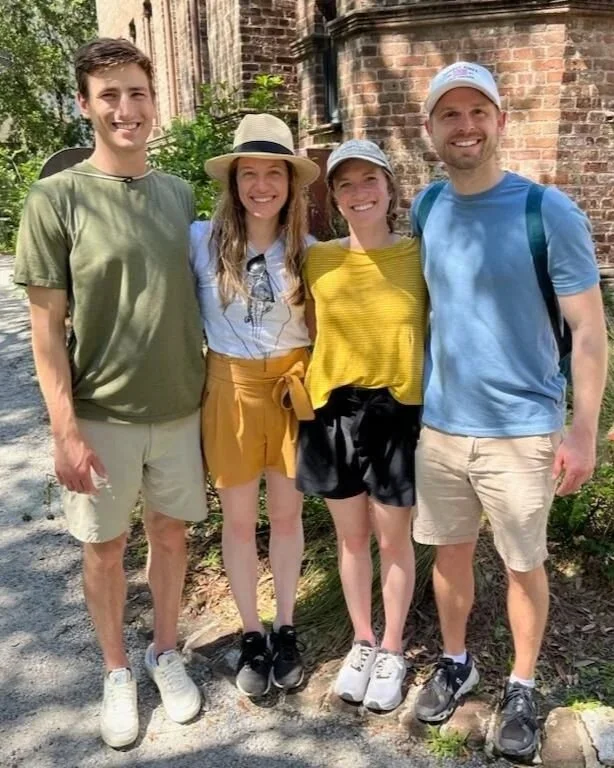 Four friends standing outdoors in front of a brick building, smiling for the camera.