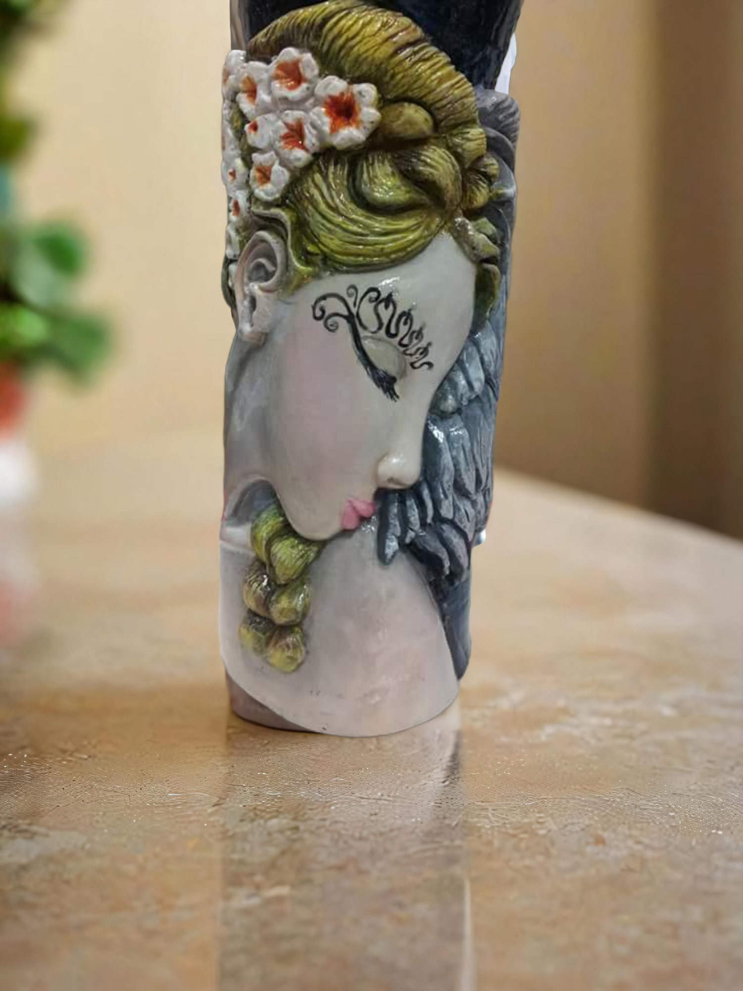 Decorative ceramic vase shaped like a woman's face with flowers in her hair, beard, and a black musical note tattoo on her cheek.