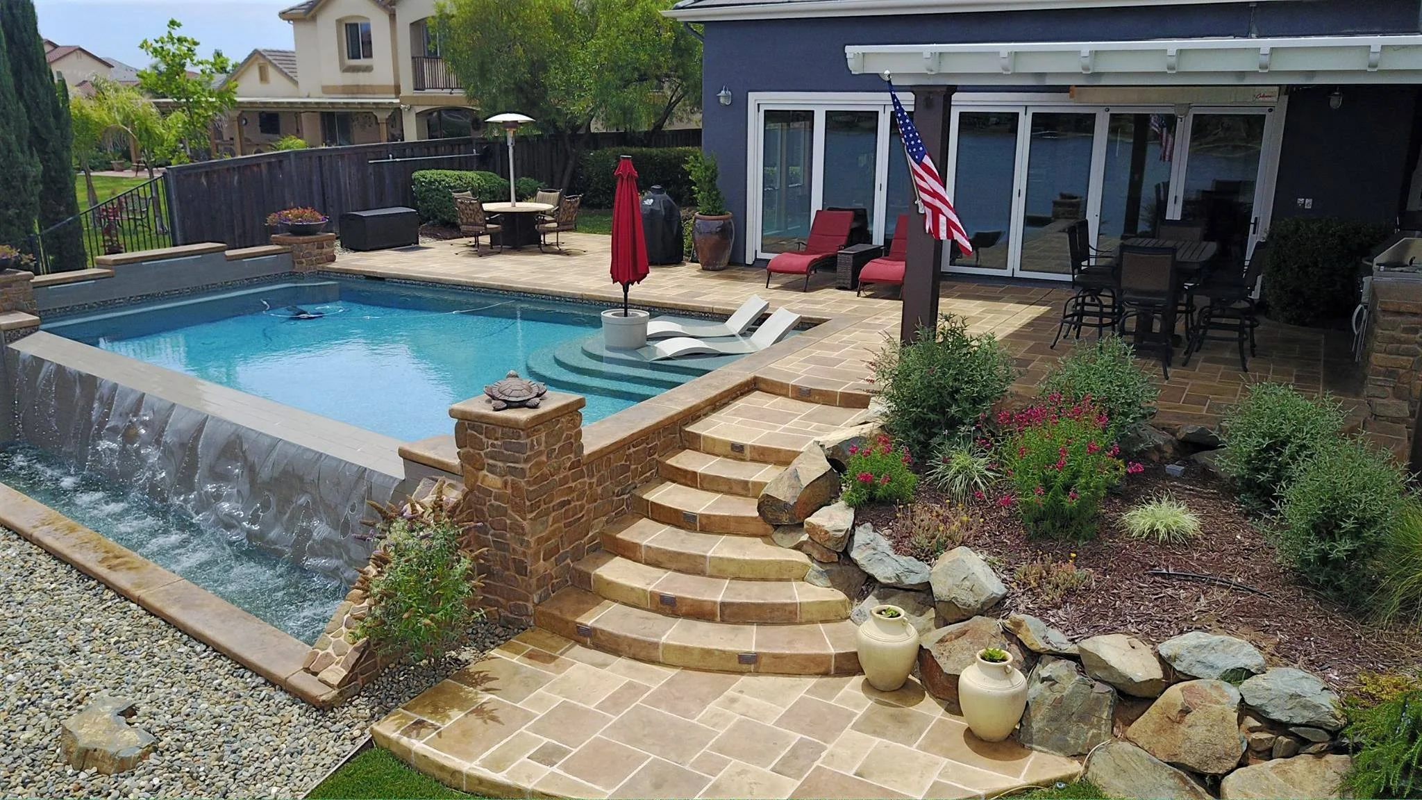 Backyard with a swimming pool, stone steps, outdoor furniture, and a landscaped garden featuring potted plants and flowers.