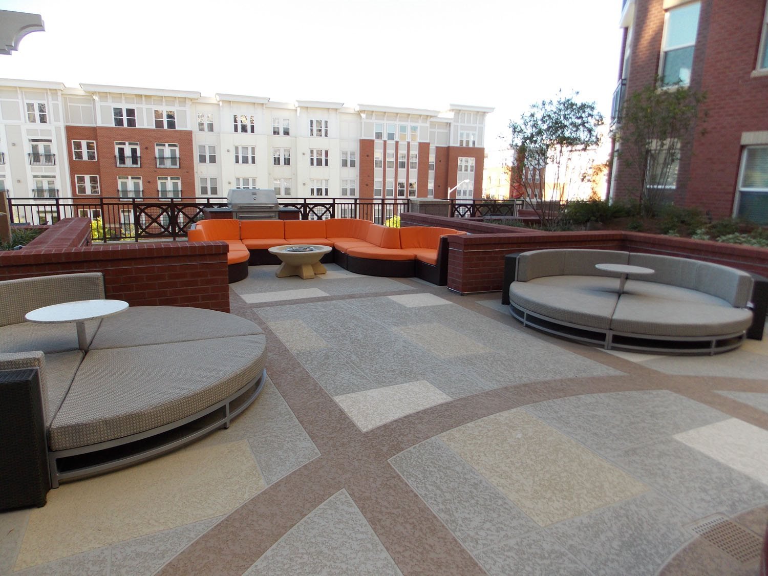 Outdoor apartment balcony with modern curved seating, a table, and a barbecue grill, overlooking other apartment buildings.