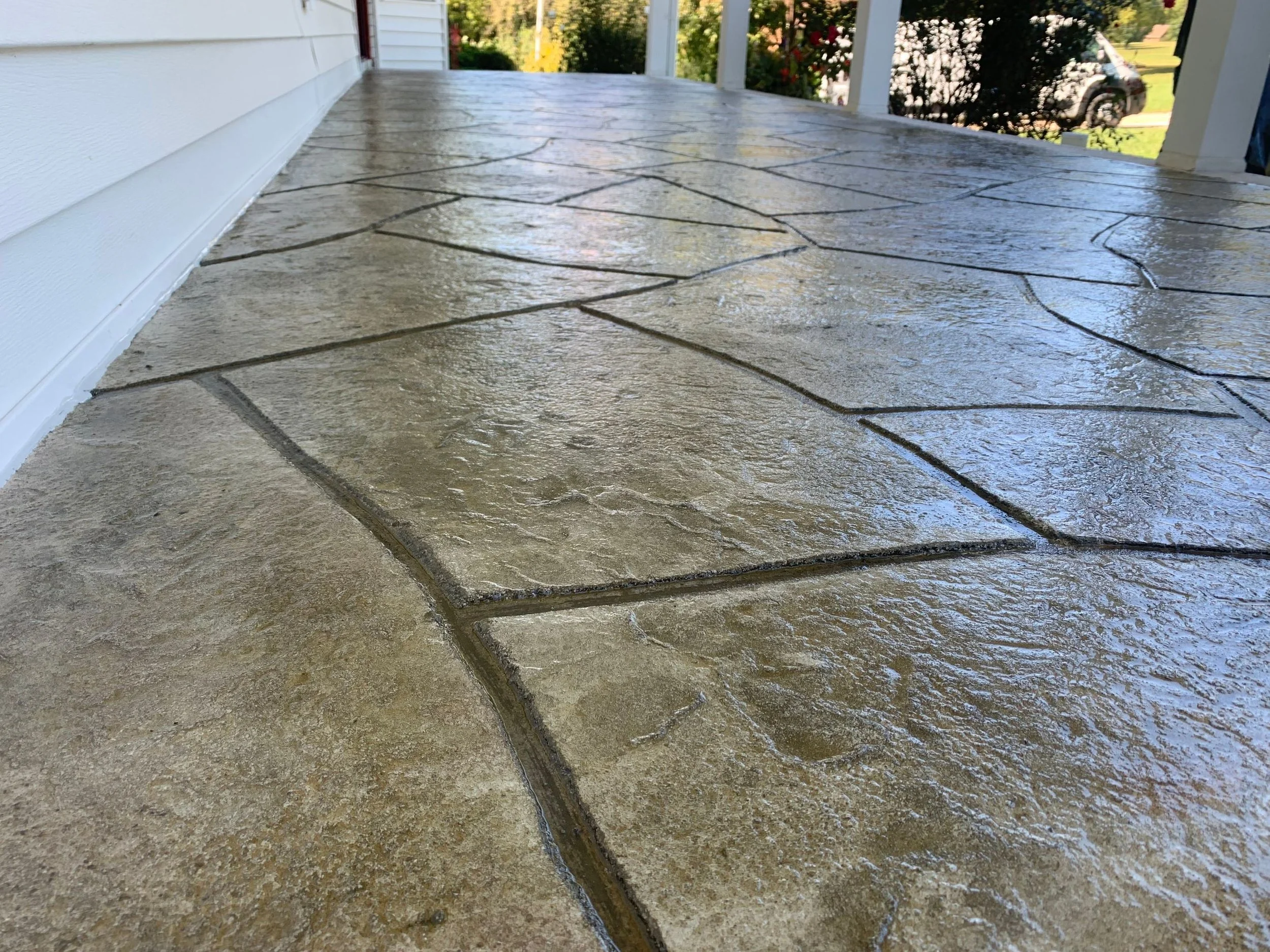 Close-up view of a wet, textured, beige stone porch floor with irregular shapes and dark grout lines, outside of a house.