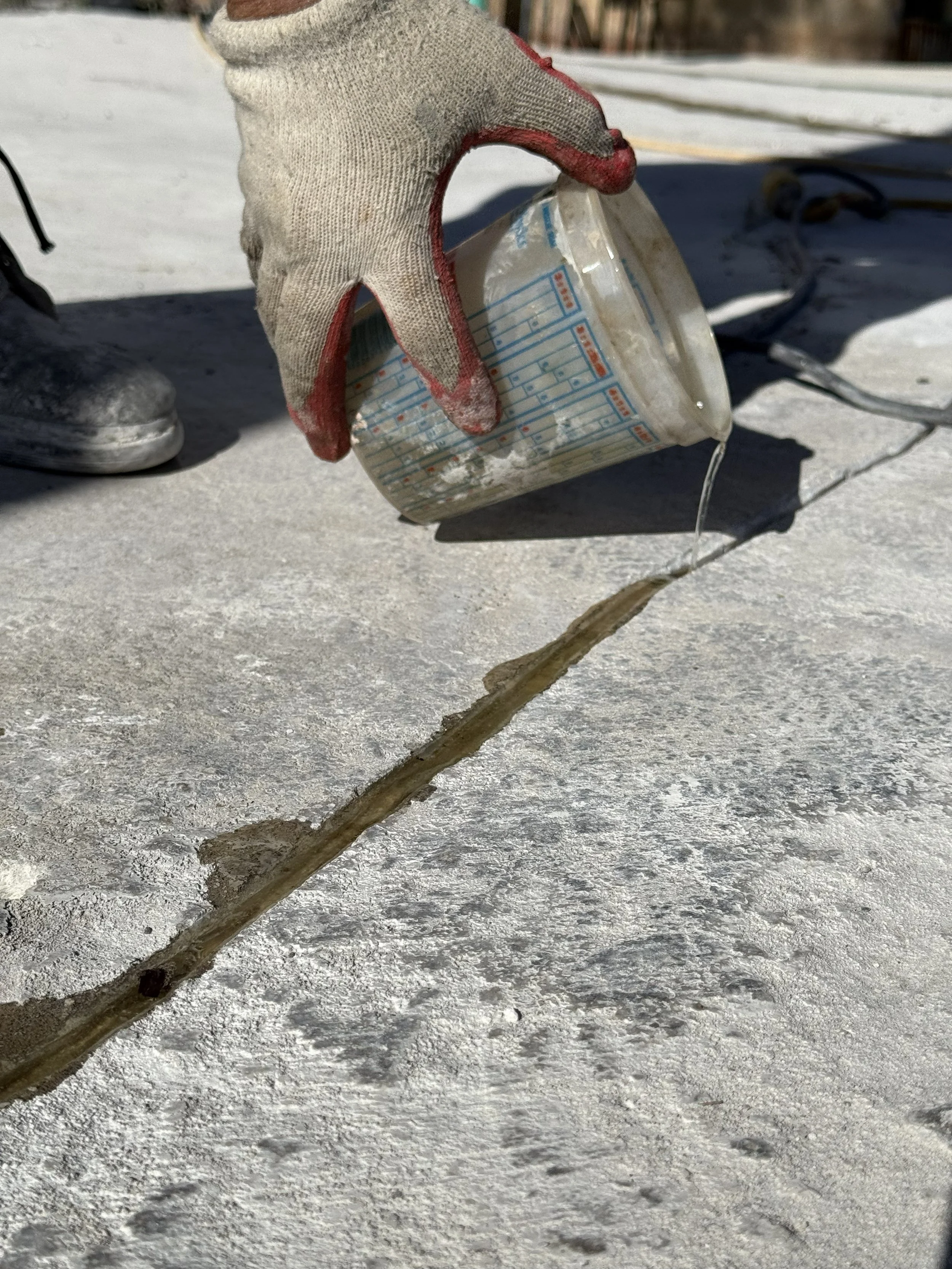 A gloved hand pouring water over a crack in an icy surface during winter.