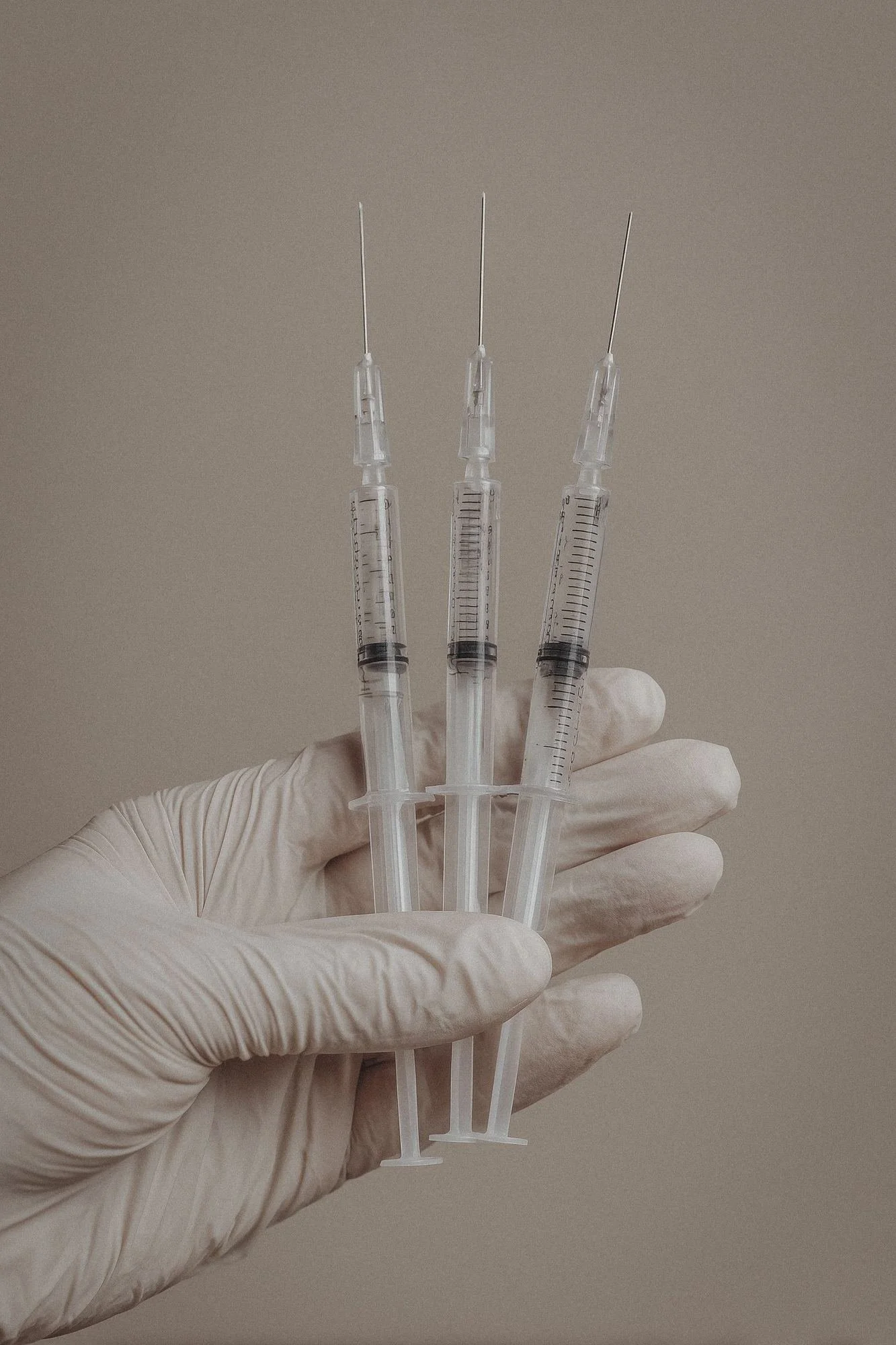 Gloved hand holding three small syringes