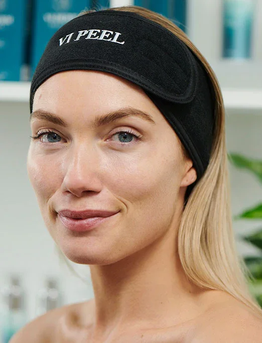 Woman wearing a black eye mask with the text 'VIP PEEL' printed on it, smiling at the camera.