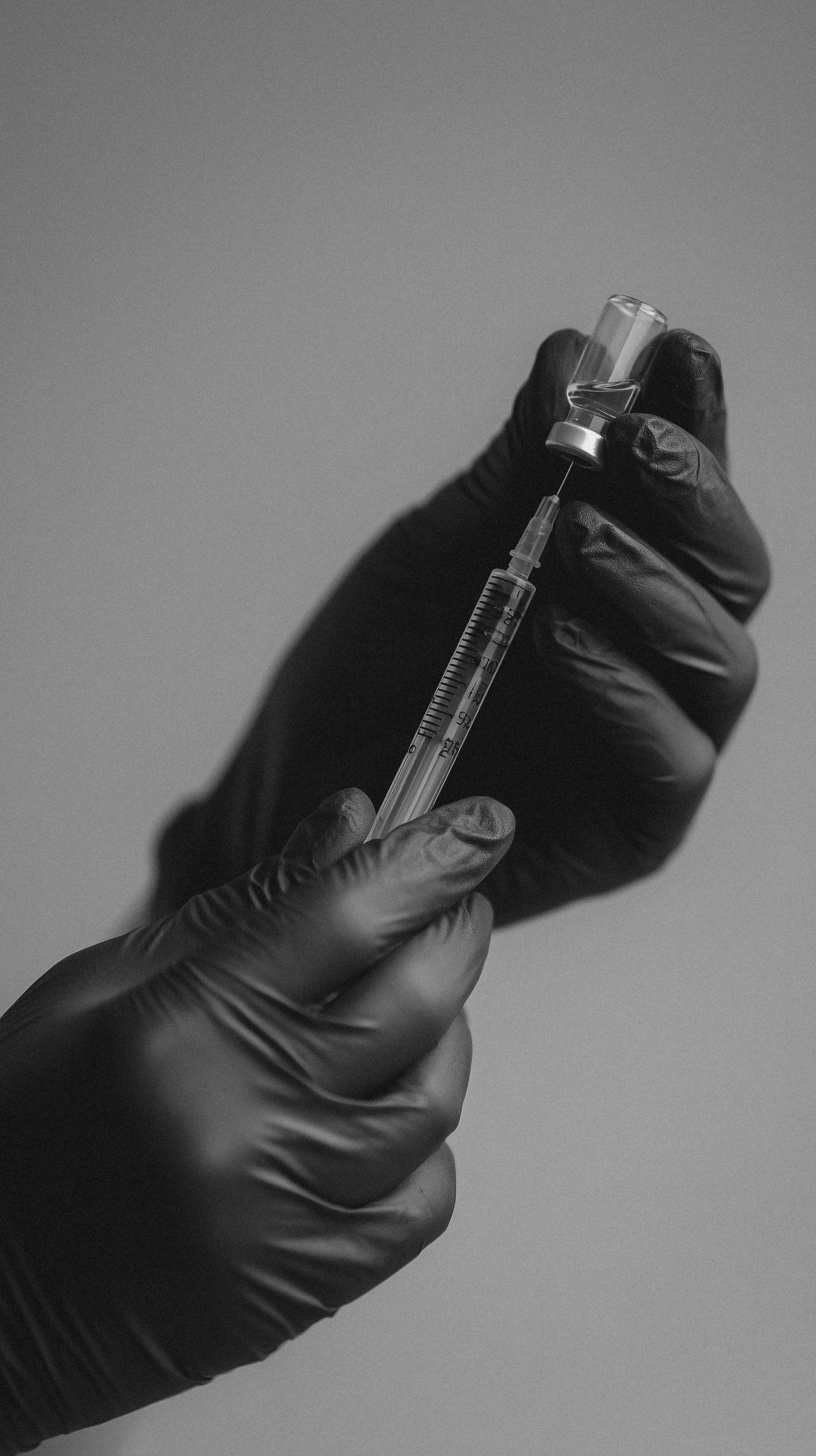 Close-up of a gloved hand holding a syringe drawing liquid from a small vial.