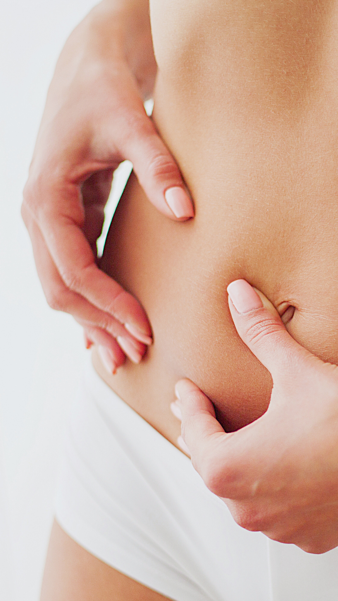 Close-up of a woman's belly with her hands forming a heart shape around her navel.