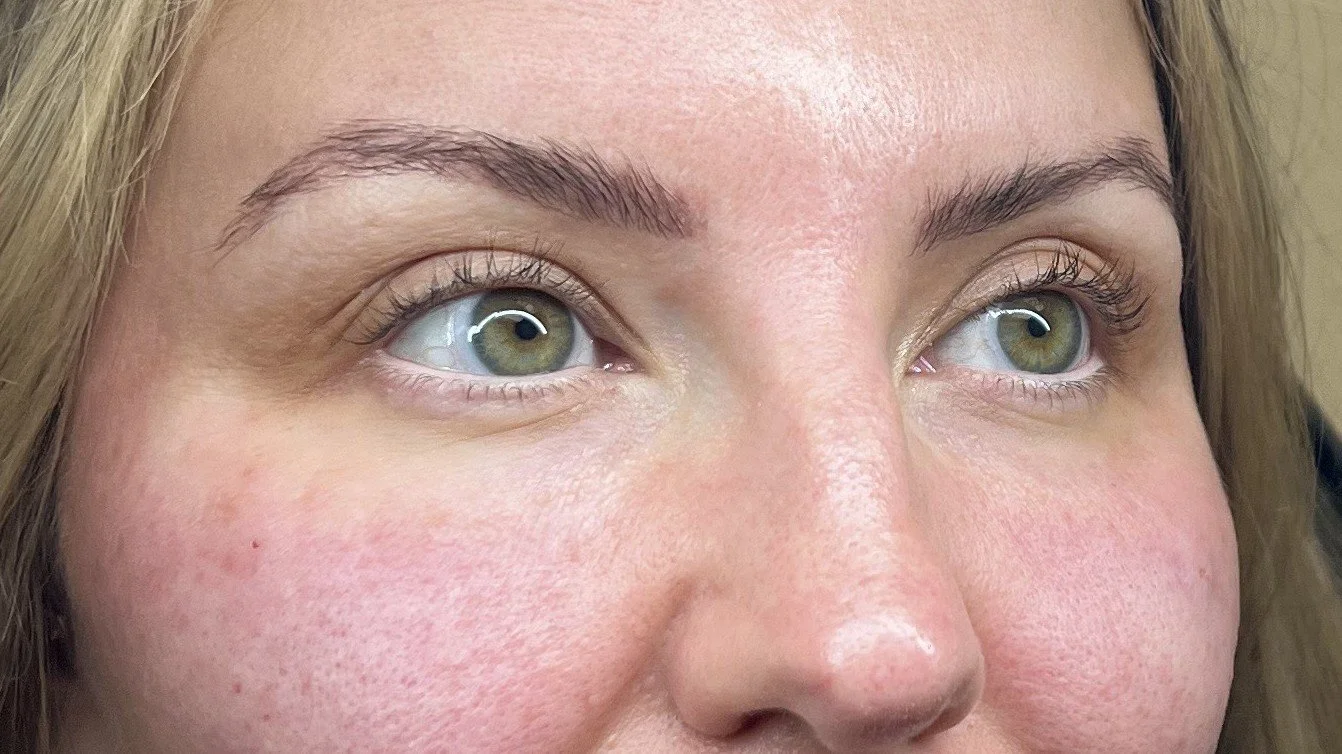 Close-up of a woman's face showing her green eyes, eyebrows, and parts of her nose and cheeks.