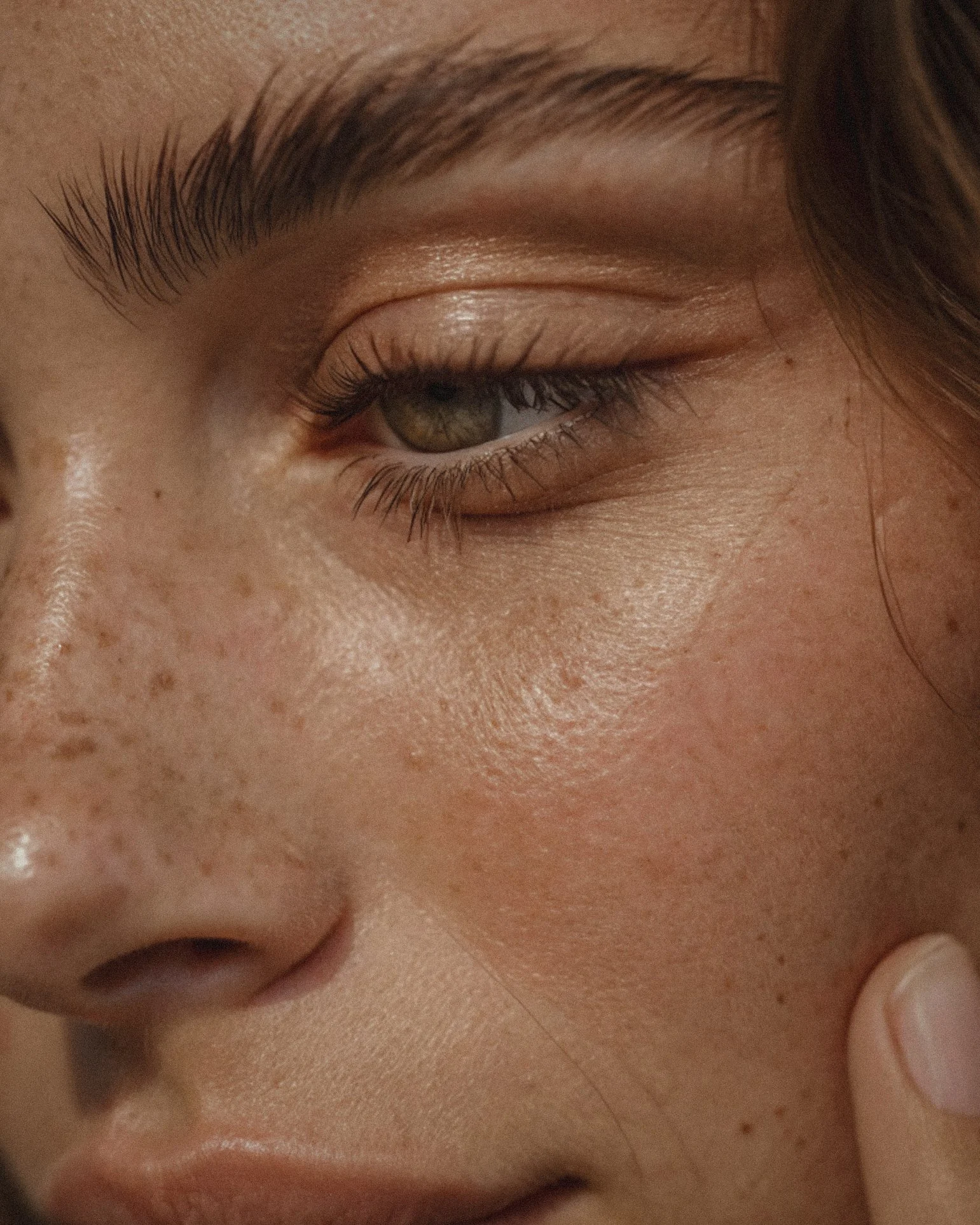 Close-up of a person's face, showing their eye, eyebrow, nose, and freckles.
