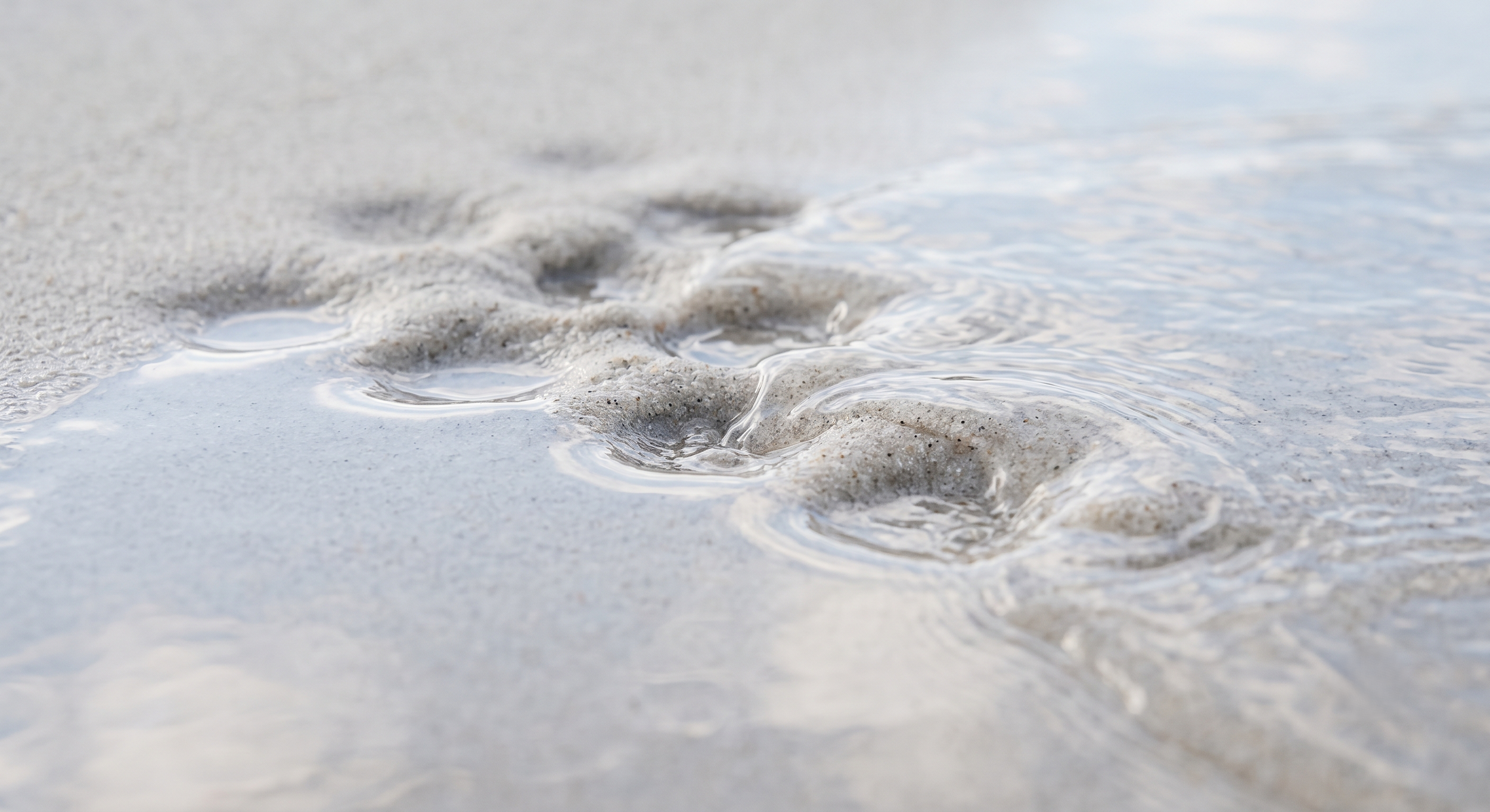 Water smoothing dimples in sand, a metaphor for collagen filling depressed acne scars from below.