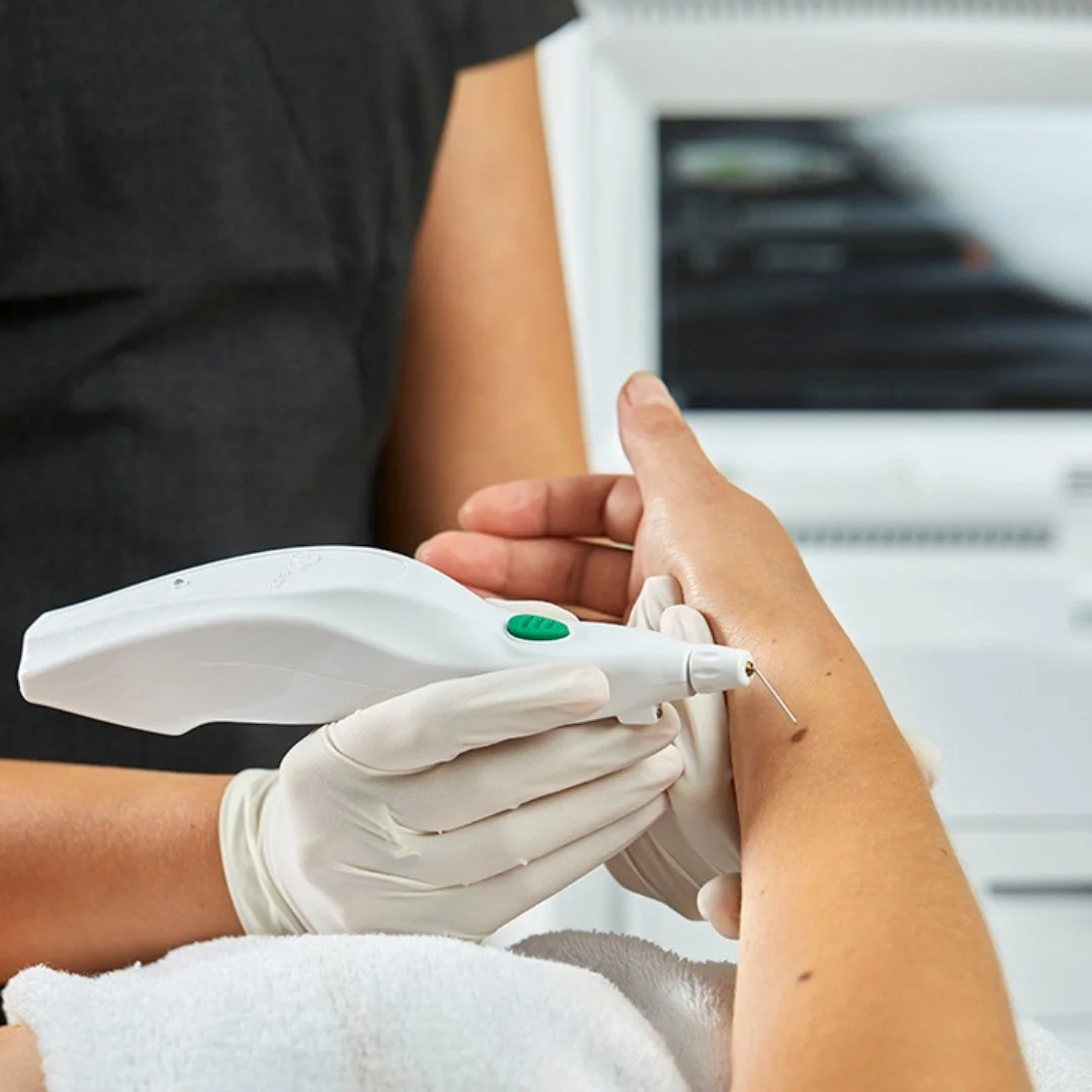 A medical professional uses a laser device on a patient's knee in a clinical setting.