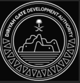 Seal for the Diriyah Gate Development Authority featuring an illustration of a historic site with a palm tree, crossed swords, and a body of water, surrounded by a circular border with geometric patterns.
