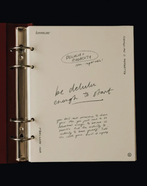Open ring binder planner with handwritten notes on a white page, including the words 'DELLUM + HOODIAC' and 'be deliberate enough to start'.