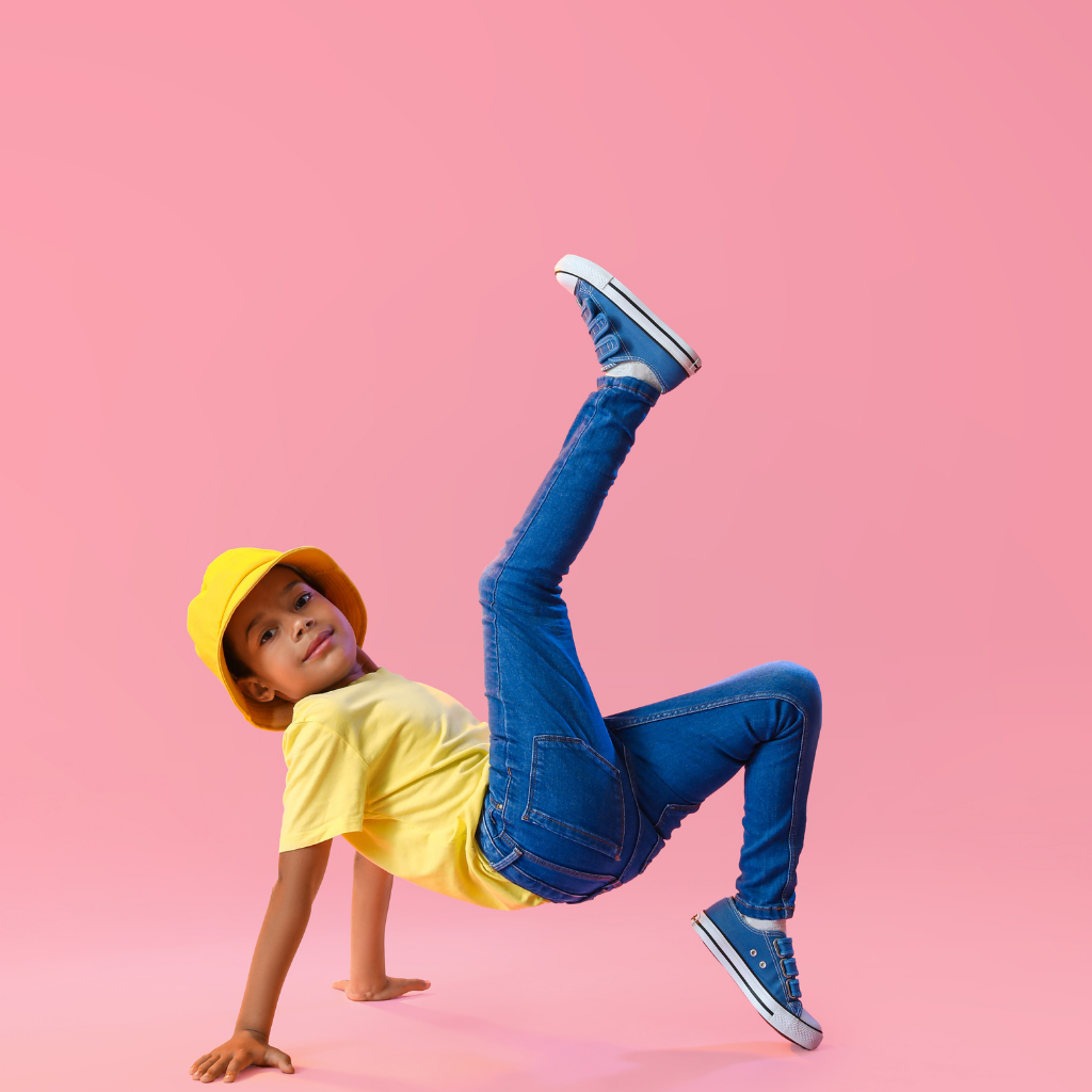 Young girl in yellow shirt and hat doing a handstand on pink background