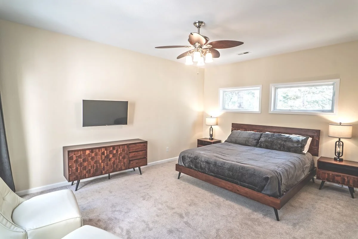 Bedroom with beige walls, gray bedding, wooden furniture, and two small horizontal windows