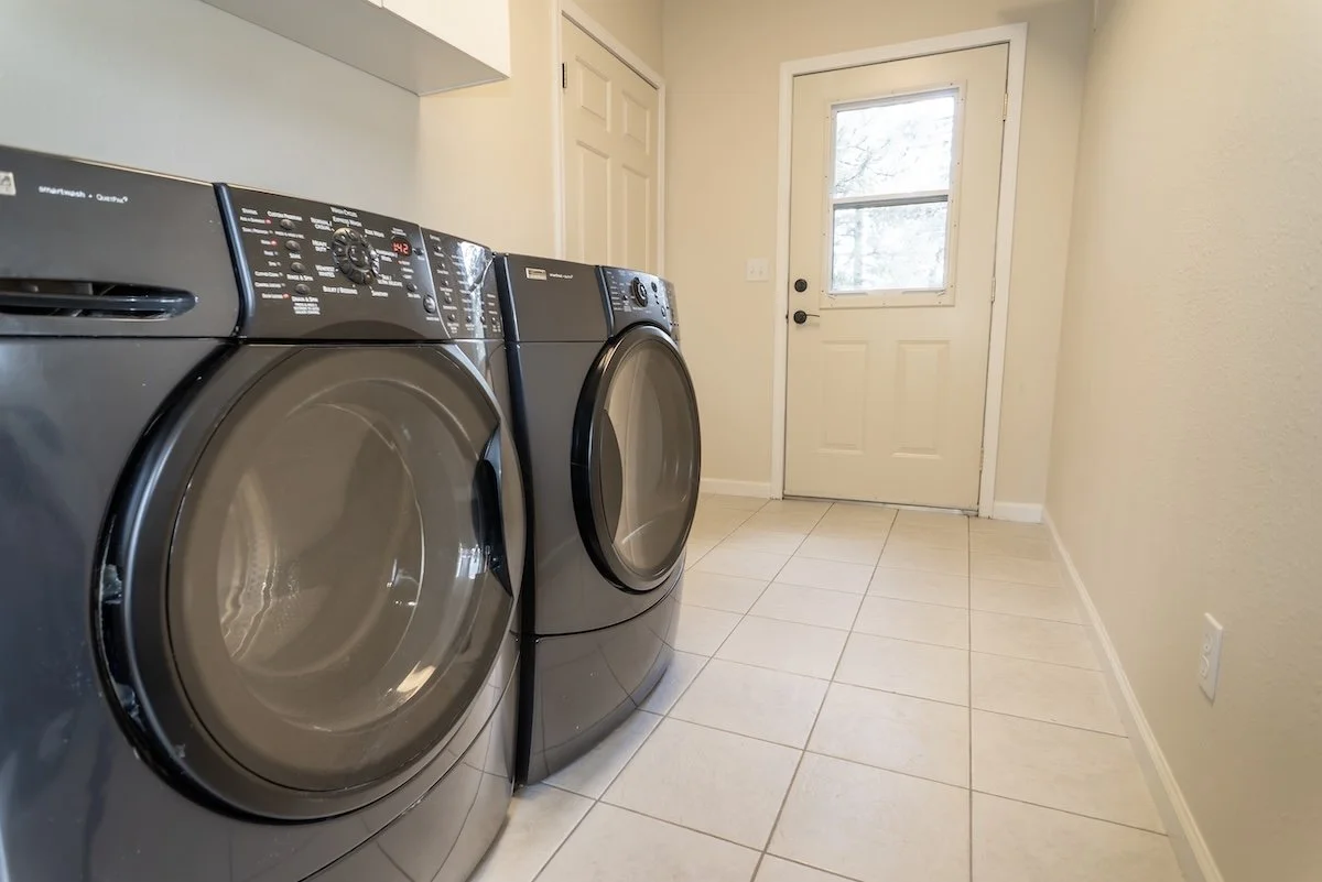 Laundry room with a front-loading washer and dryer in a neutral-colored space with a door and tiled floor.