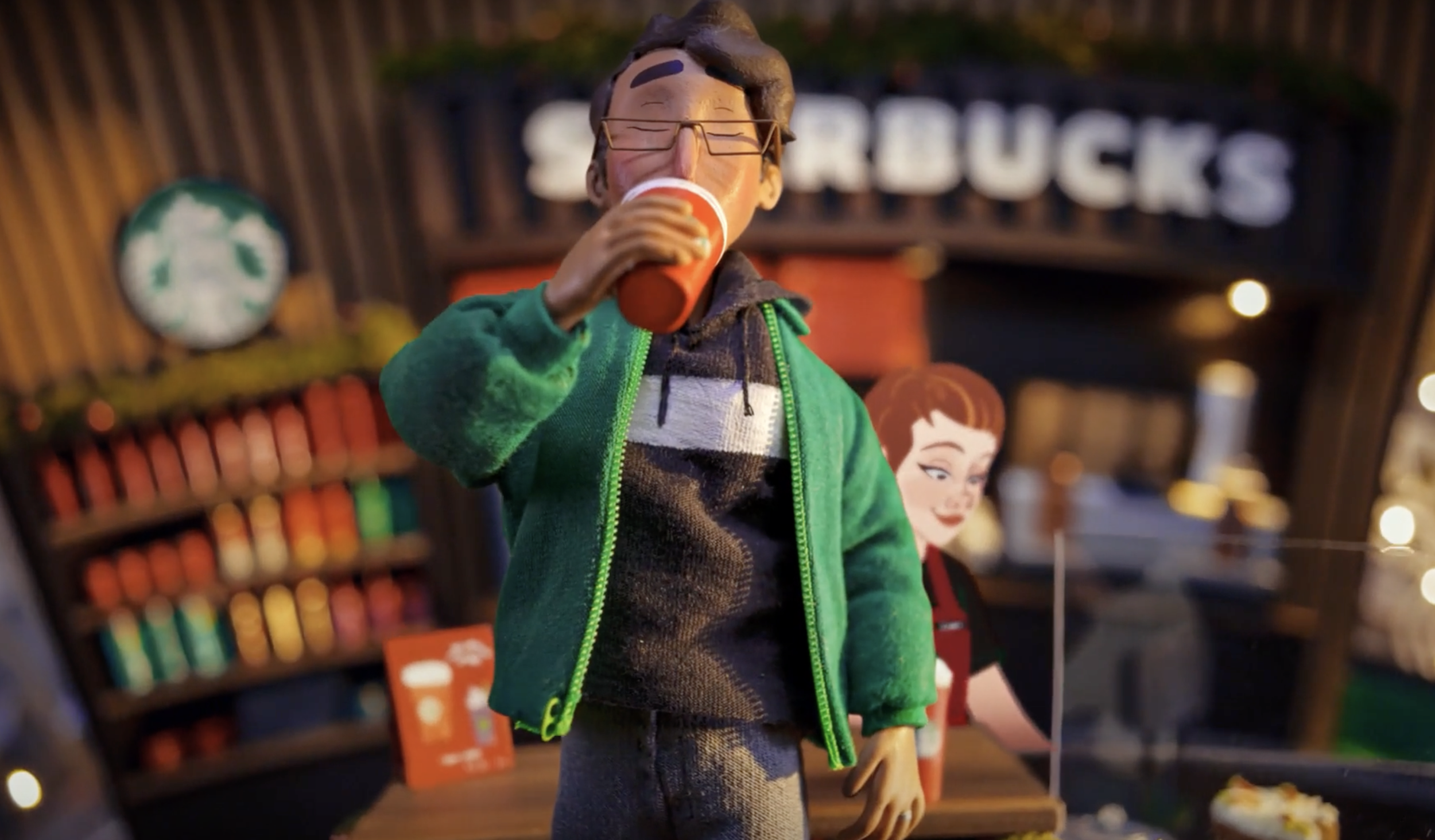A detailed figurine of a man wearing glasses, a green hoodie, and a hoodie, drinking from a red cup inside a Starbucks store.