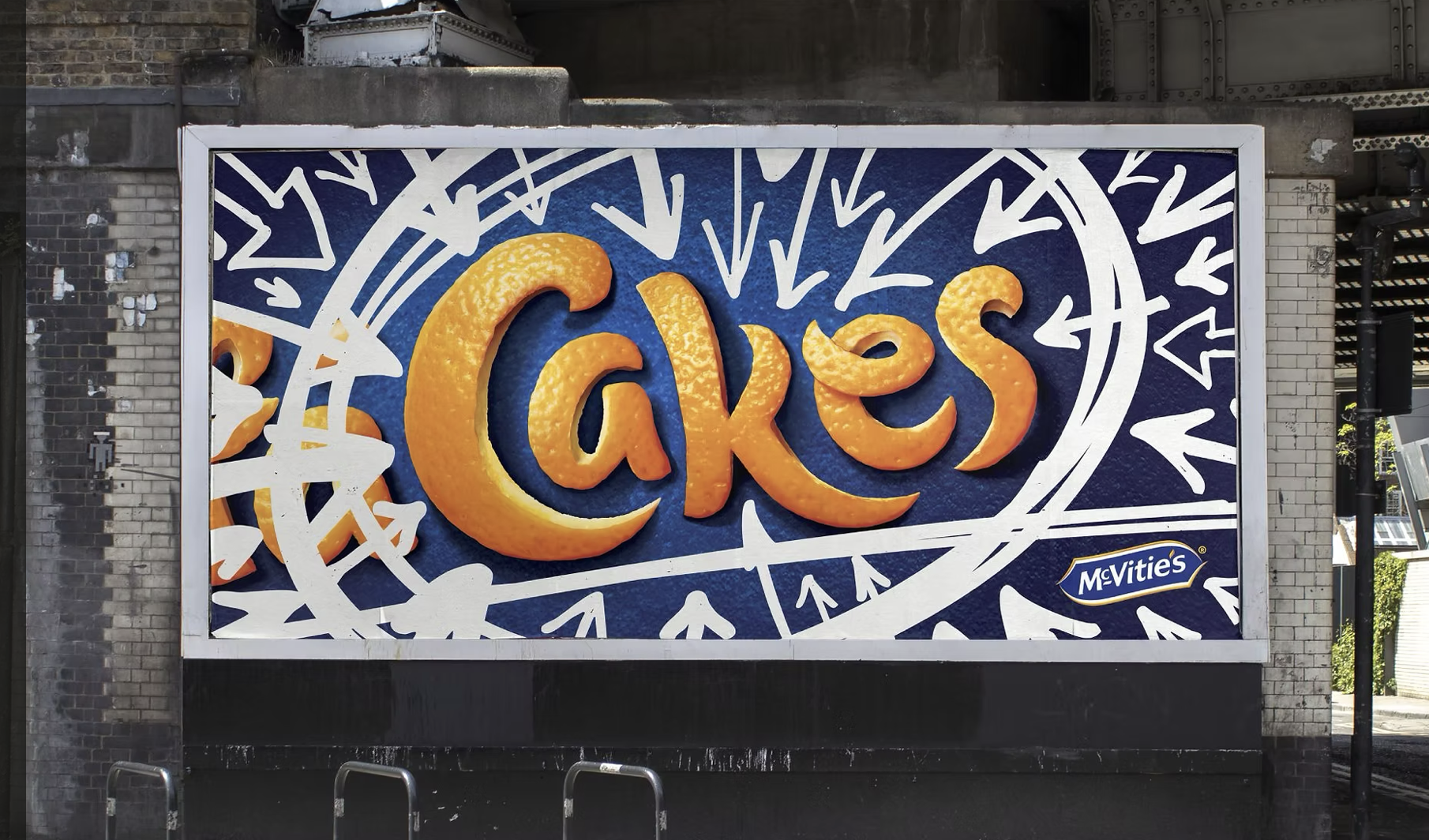 Billboard advertisement for Cakes by McVitie's with a large stylized orange peel-textured cake logo on a blue background with white arrows and circles.