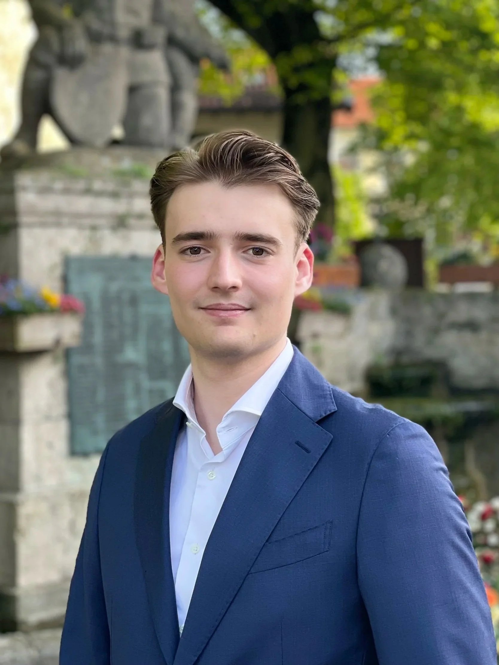 Lukas a cybersecurity architect in a blue suit and white shirt standing outdoors with a blurred greenery.