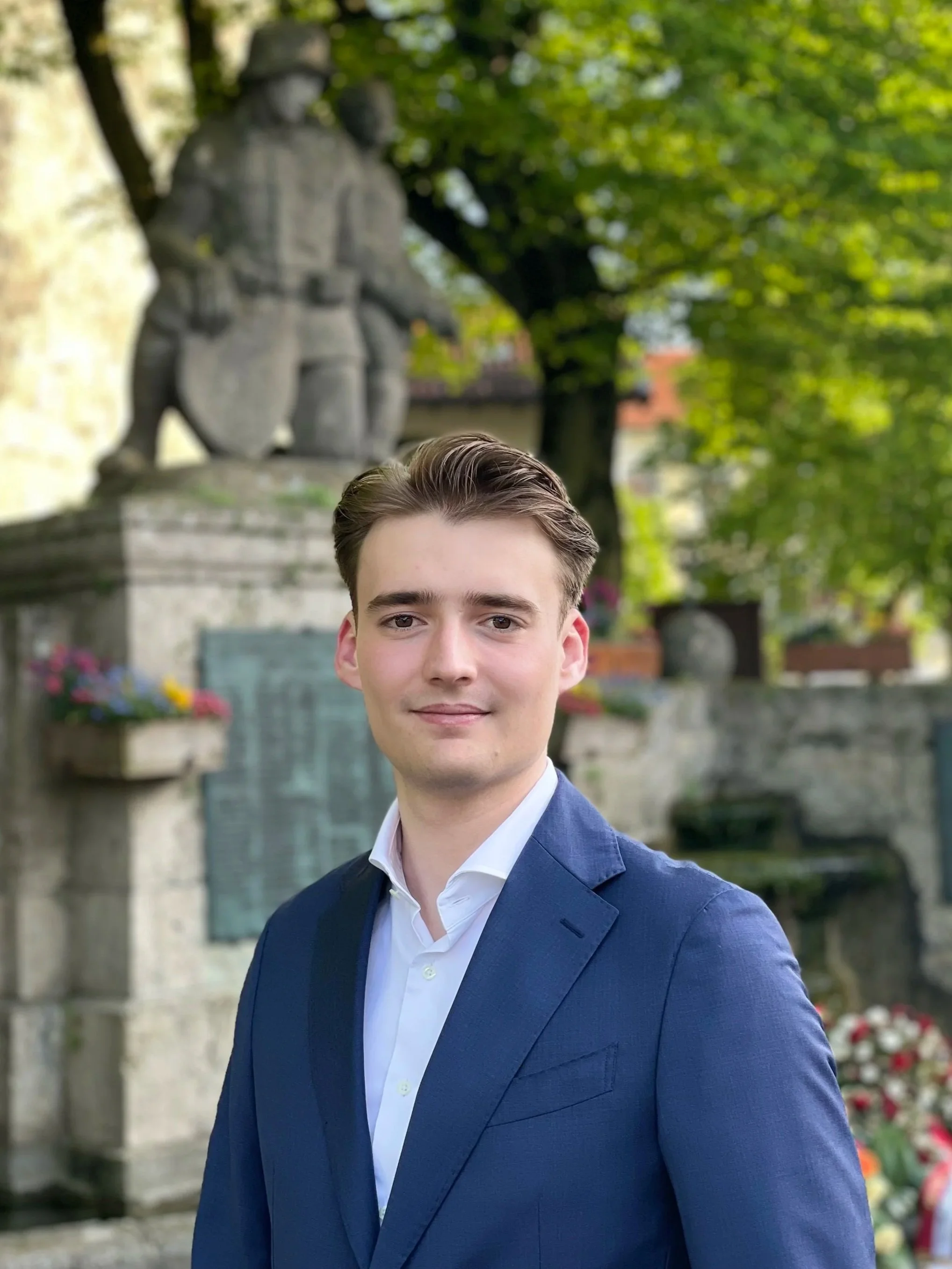 Lukas a cybersecurity architect in a blue suit and white shirt standing outdoors with a blurred greenery.
