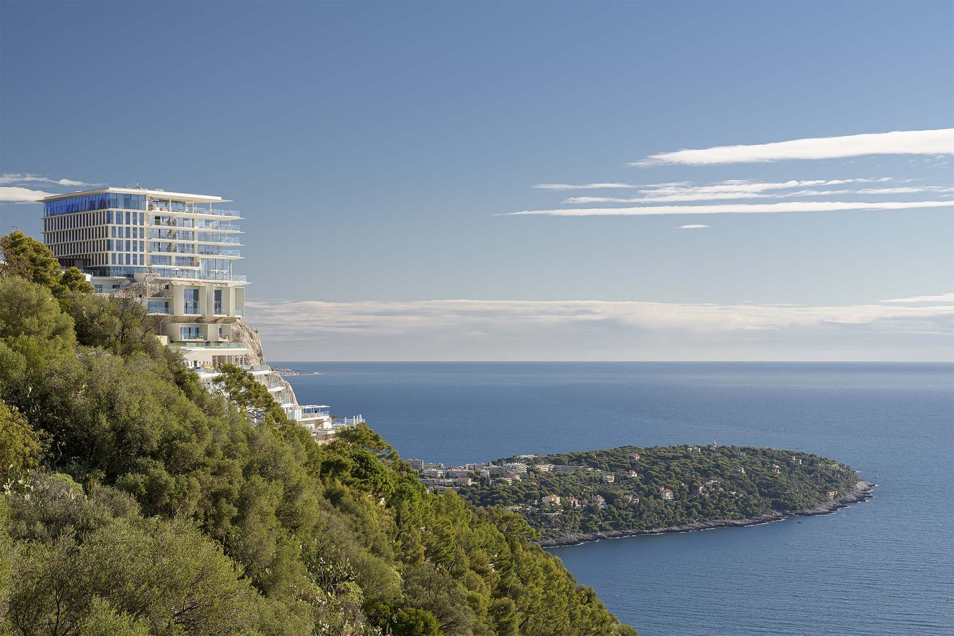 Crowd of people inside a large, well-lit room with high arched windows, some looking at clothing racks, some browsing at tables, and others chatting, with a large screen on the wall and stage lighting overhead.