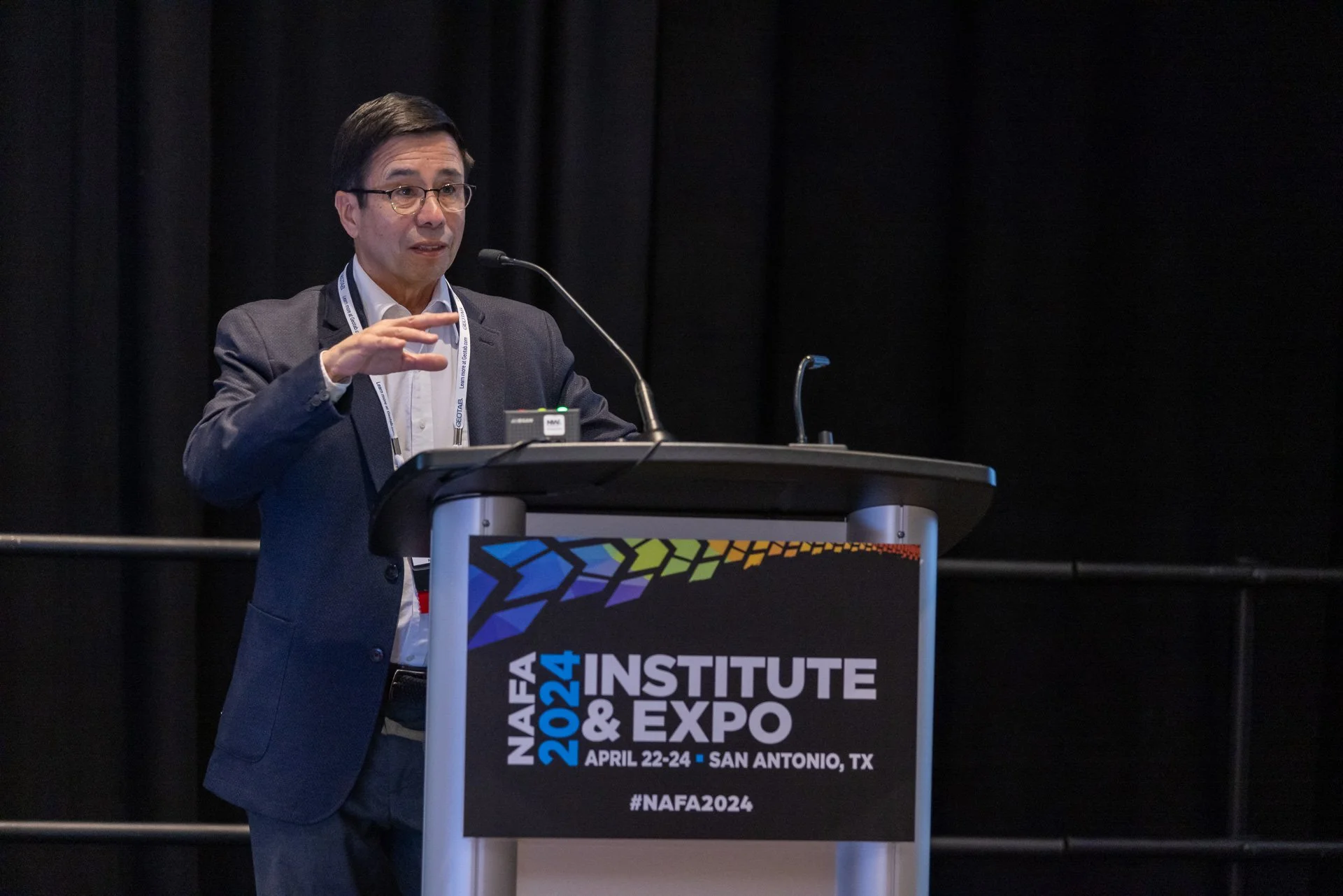 A man in a suit speaking at a conference podium with a black background. The podium has a sign for the NAFA 2024 Institute & Expo held in San Antonio, Texas, April 22-24, 2024.