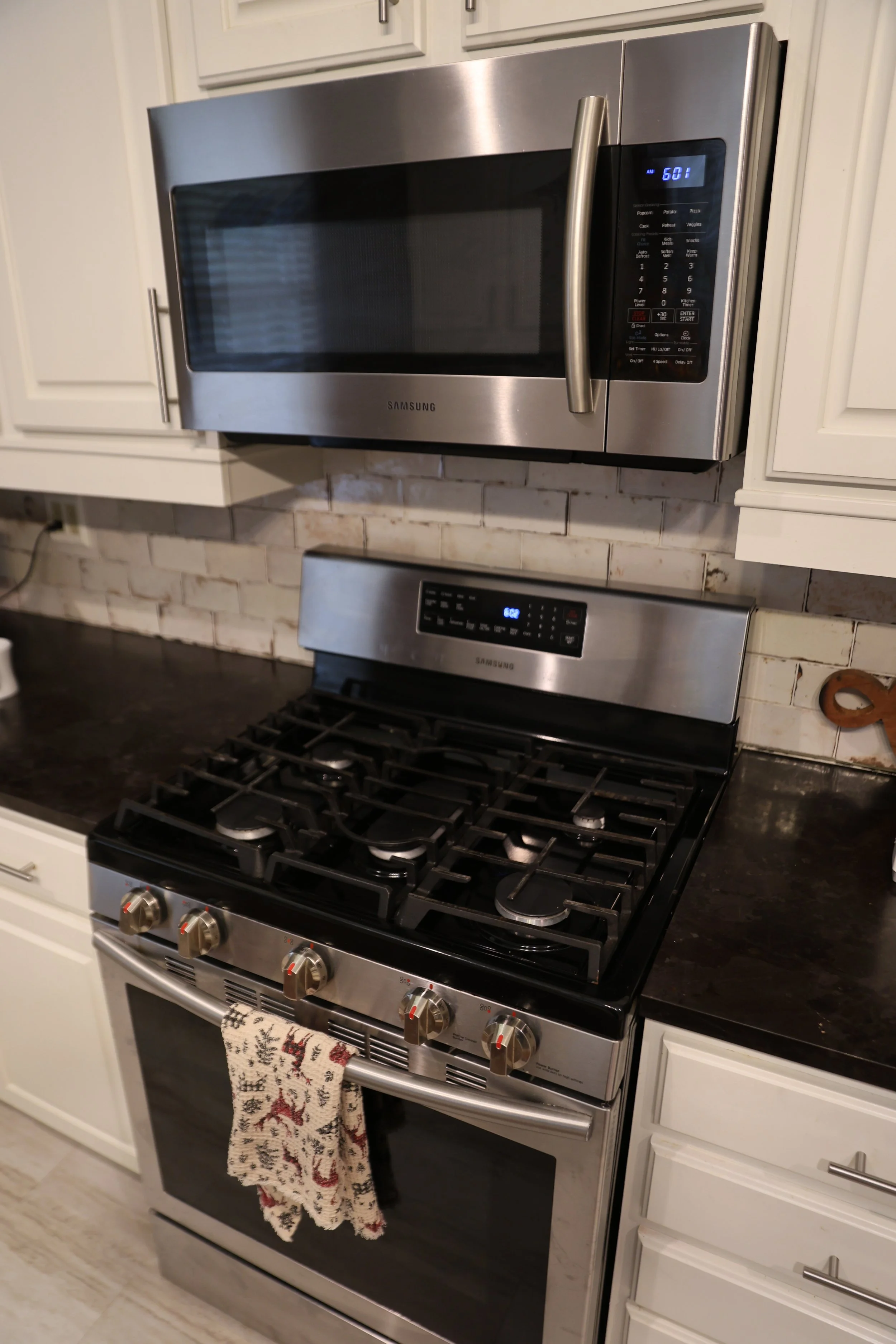 Kitchen with stainless steel microwave above stove with digital displays, black stovetop with five burners, and white cabinets with silver handles.