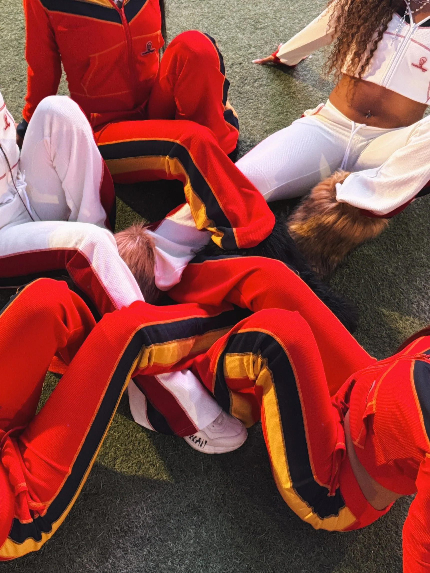 Group of people in athletic outfits sitting on the ground, one person appears to be petting a dog.