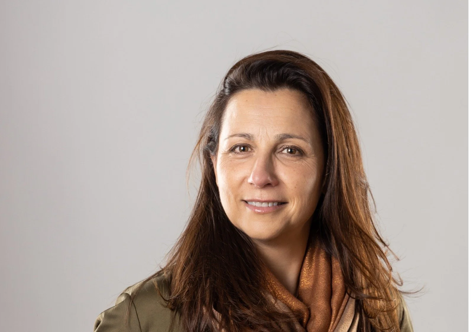 Retrato de una mujer con cabello castaño, sonriendo y con un fondo gris claro.