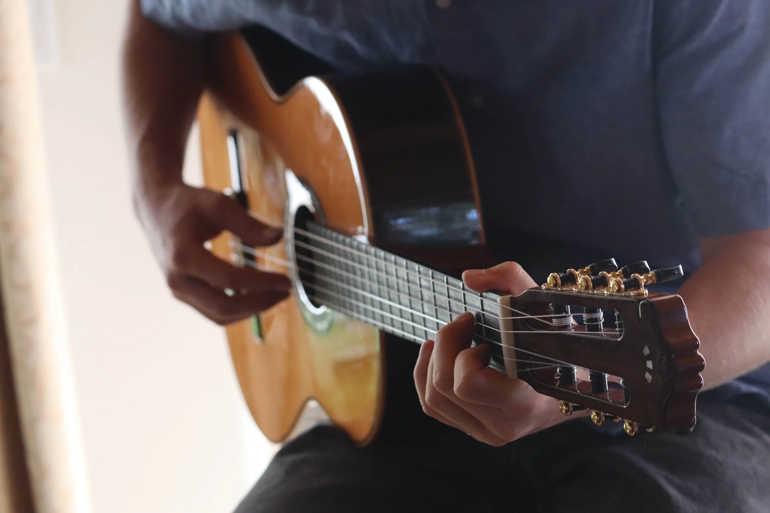 Close-up of a person playing an acoustic guitar, focusing on their hands and the guitar neck.