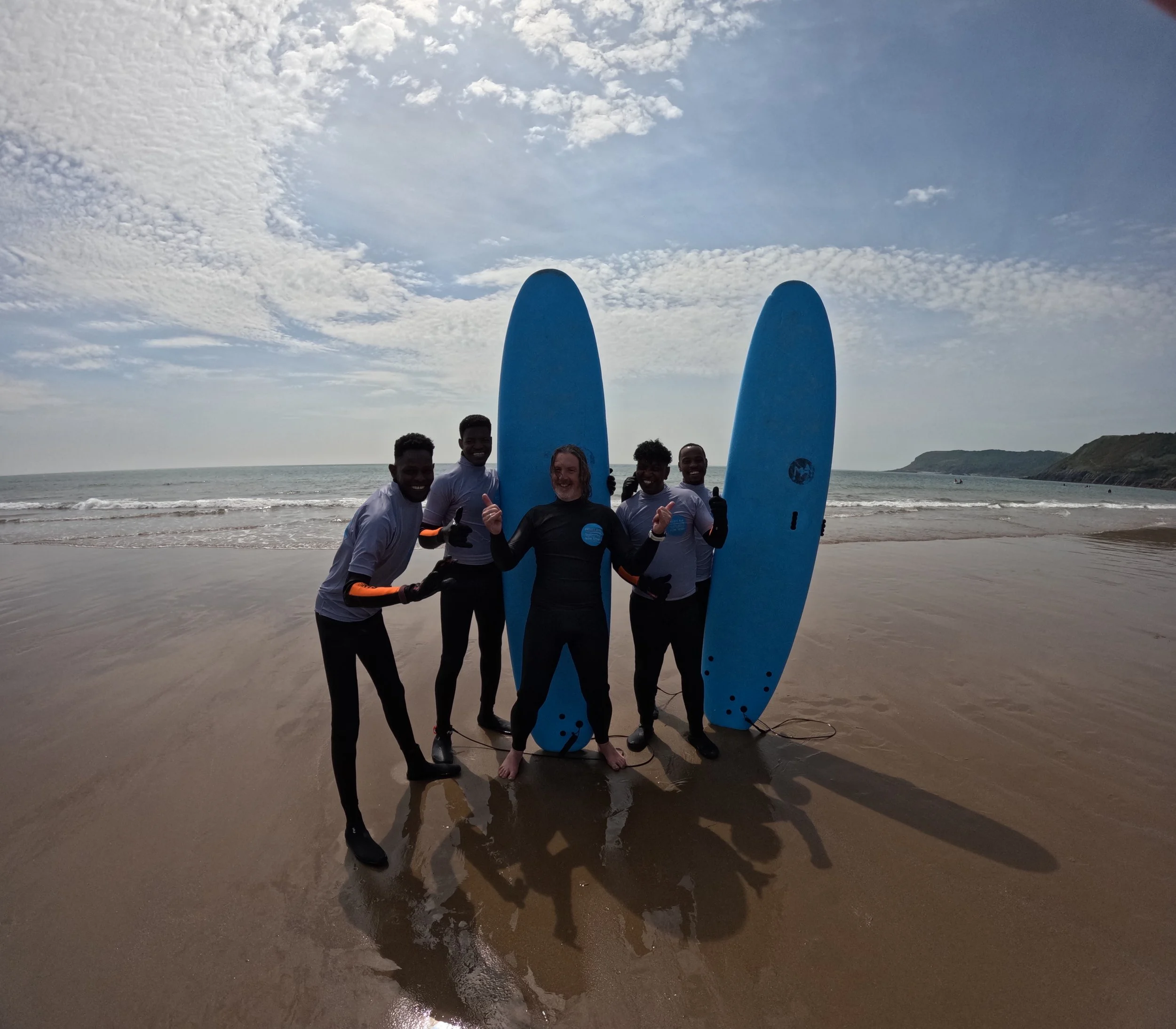 Four people on a beach with surfboards, smiling and posing for a photo.