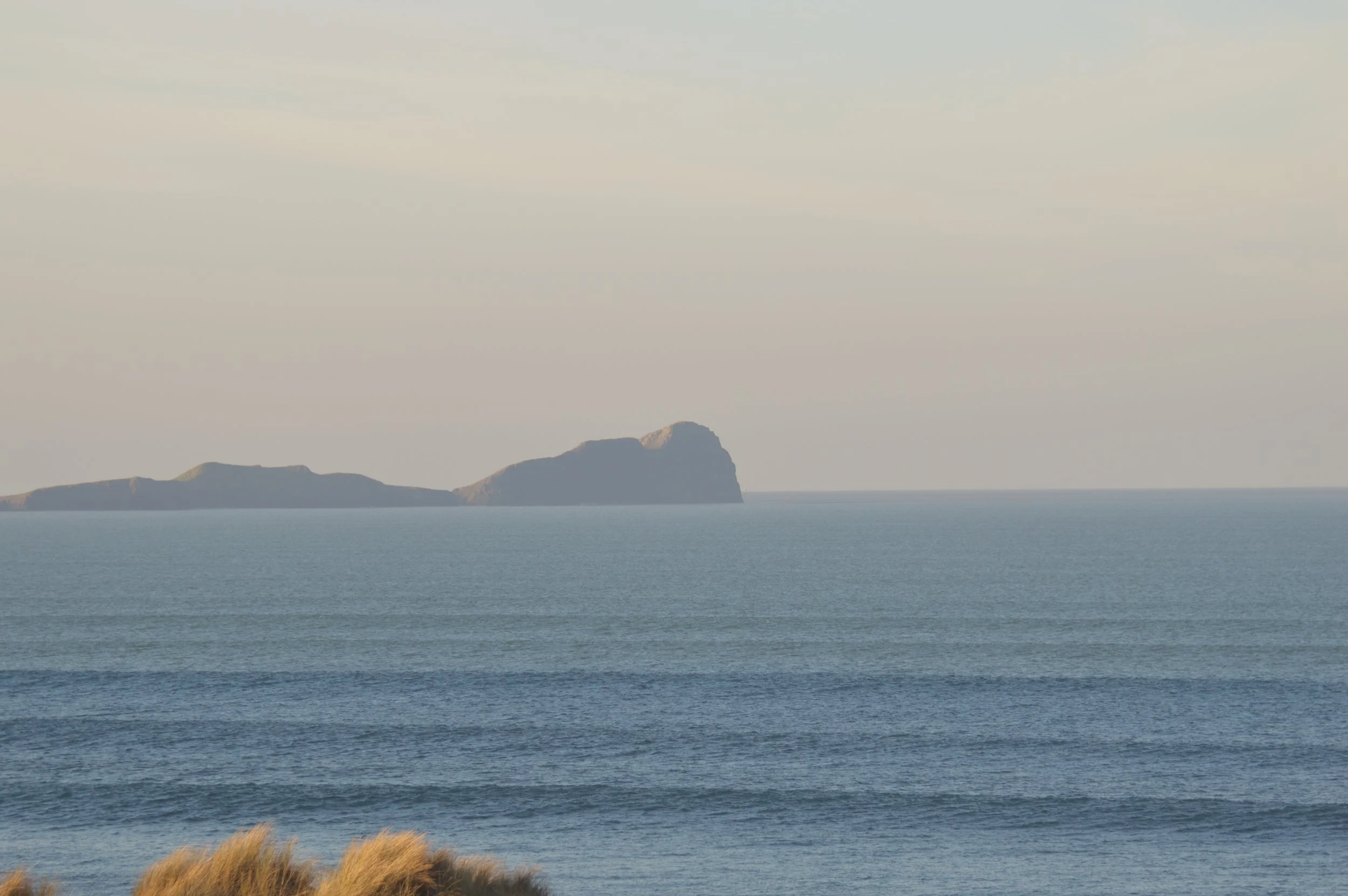 A seascape showing a calm ocean with a distant island or landmass on the horizon under a partly cloudy sky.