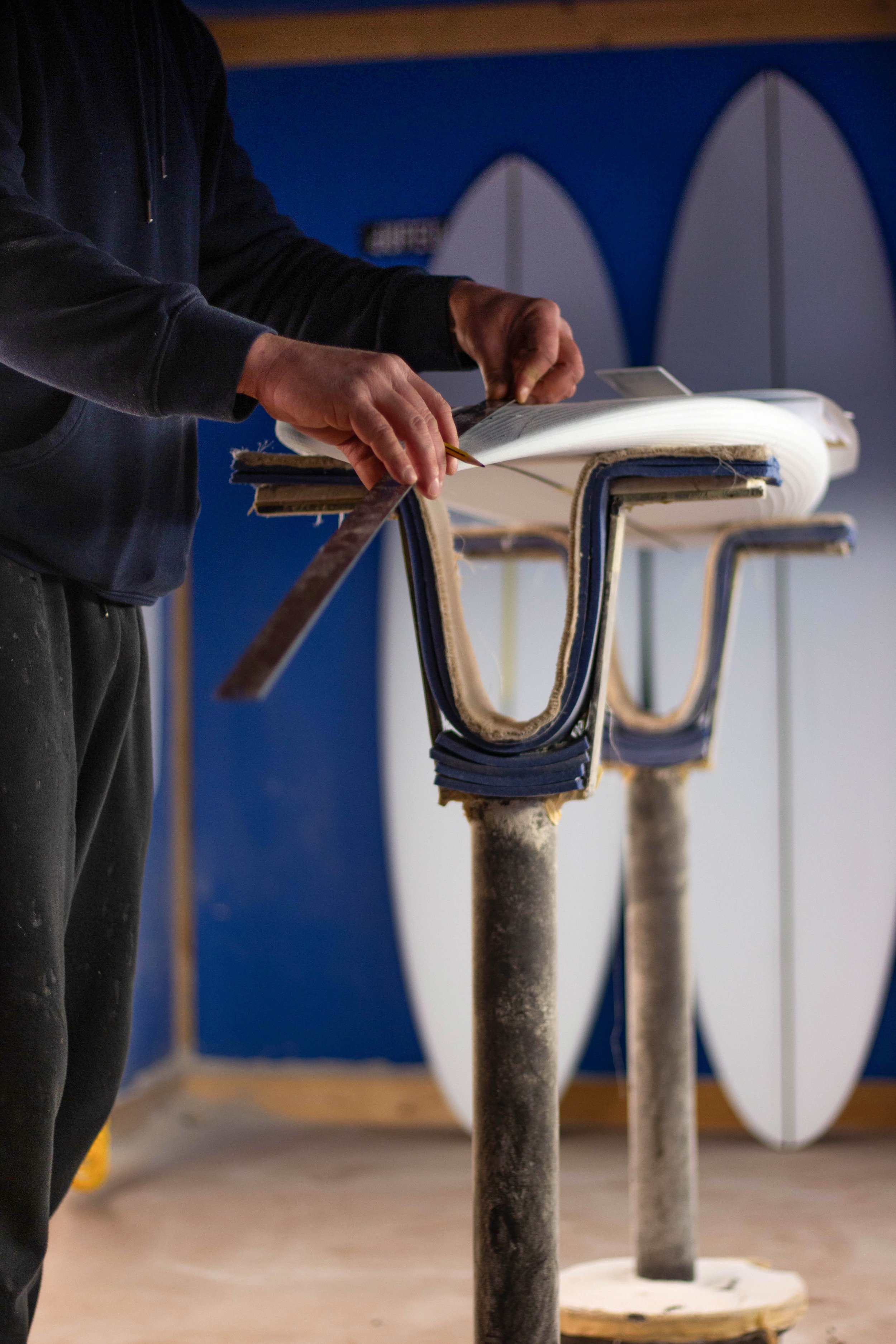 A person working on a surfboard inside a workshop, with surfboards in the background.